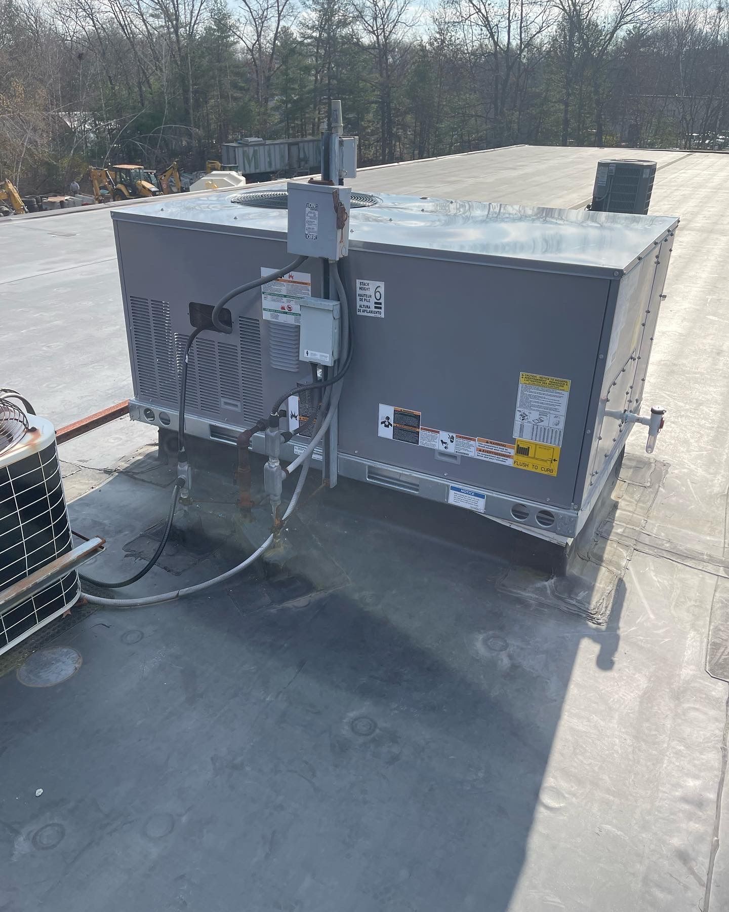 Rooftop HVAC unit on a flat, black roof. Gray metal box with attached pipes and electrical components.