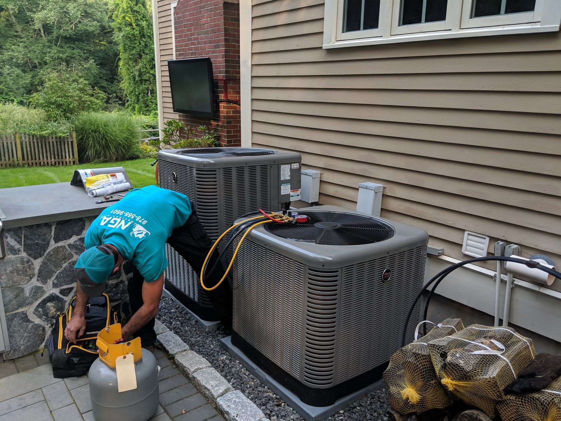 HVAC technician working on outdoor air conditioning units near a house.