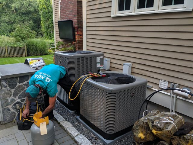 HVAC technician working on outdoor air conditioning units near a house.