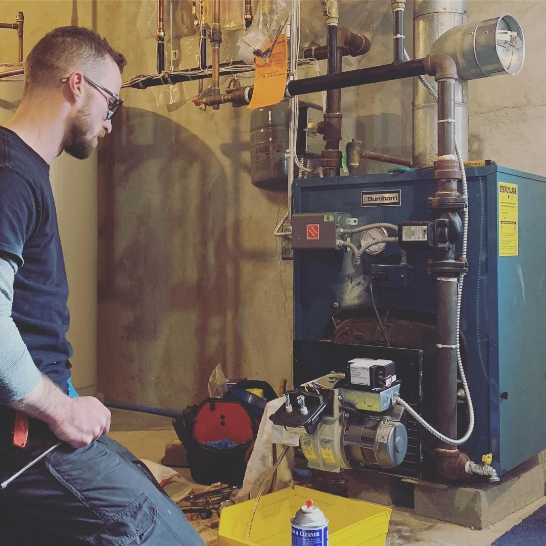 Man examining a furnace in a basement. He holds a tool and wears glasses.