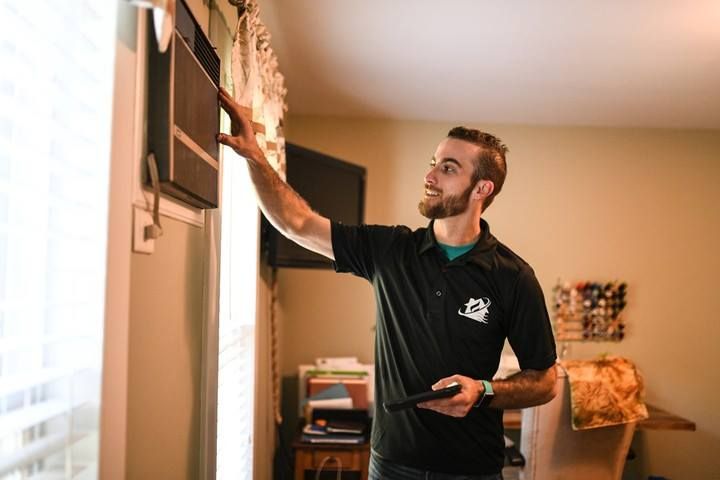 Man adjusting an air conditioner in a home, holding a tablet.