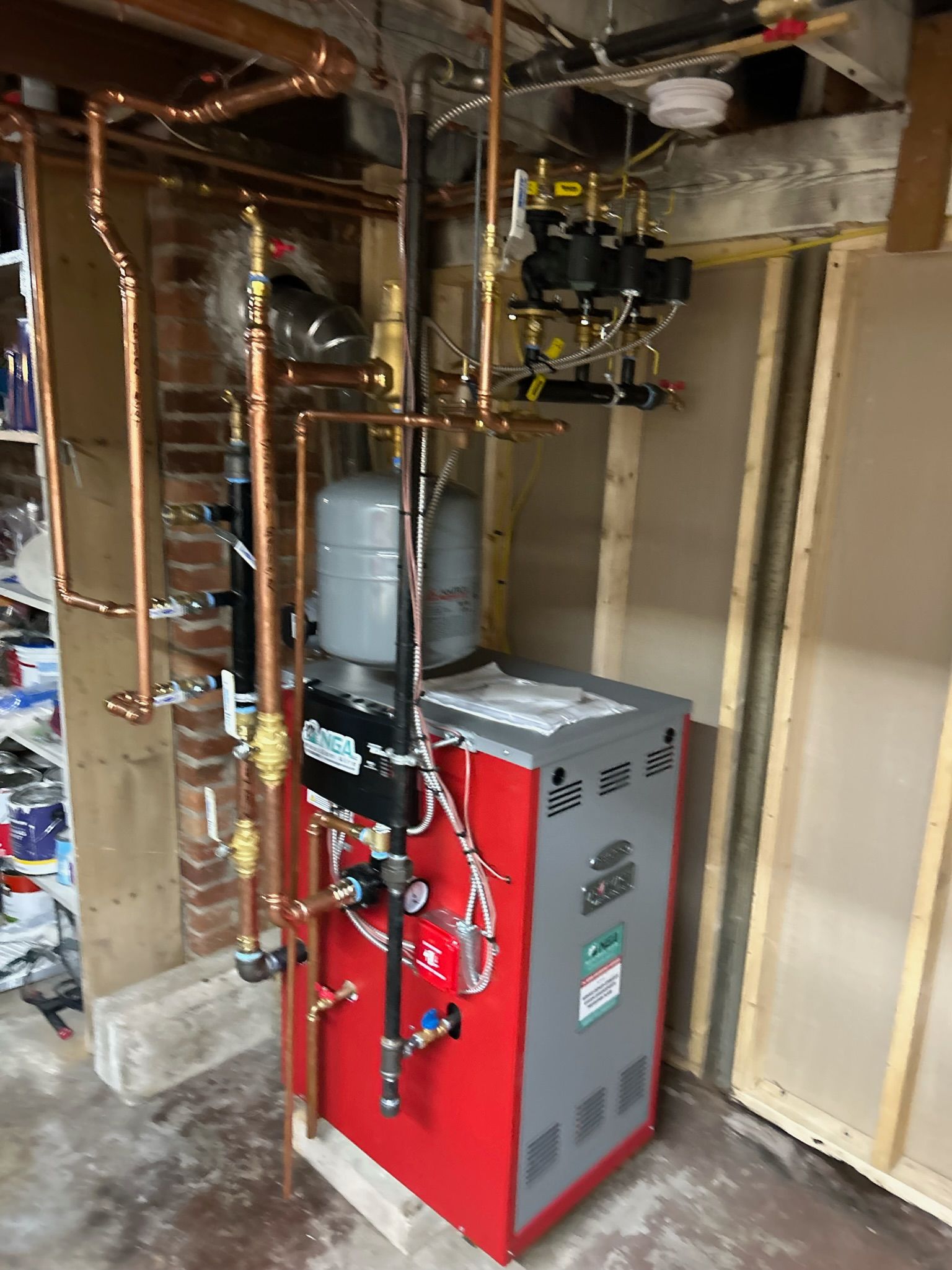 A red and gray boiler with copper pipes installed against a wooden wall.