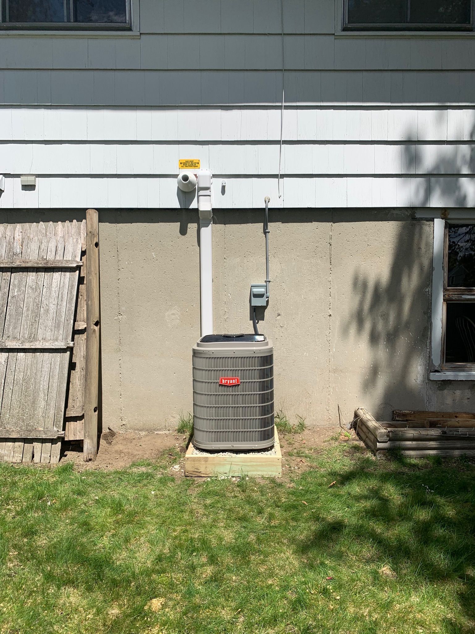 Exterior HVAC unit against a concrete foundation, white siding, and green grass.
