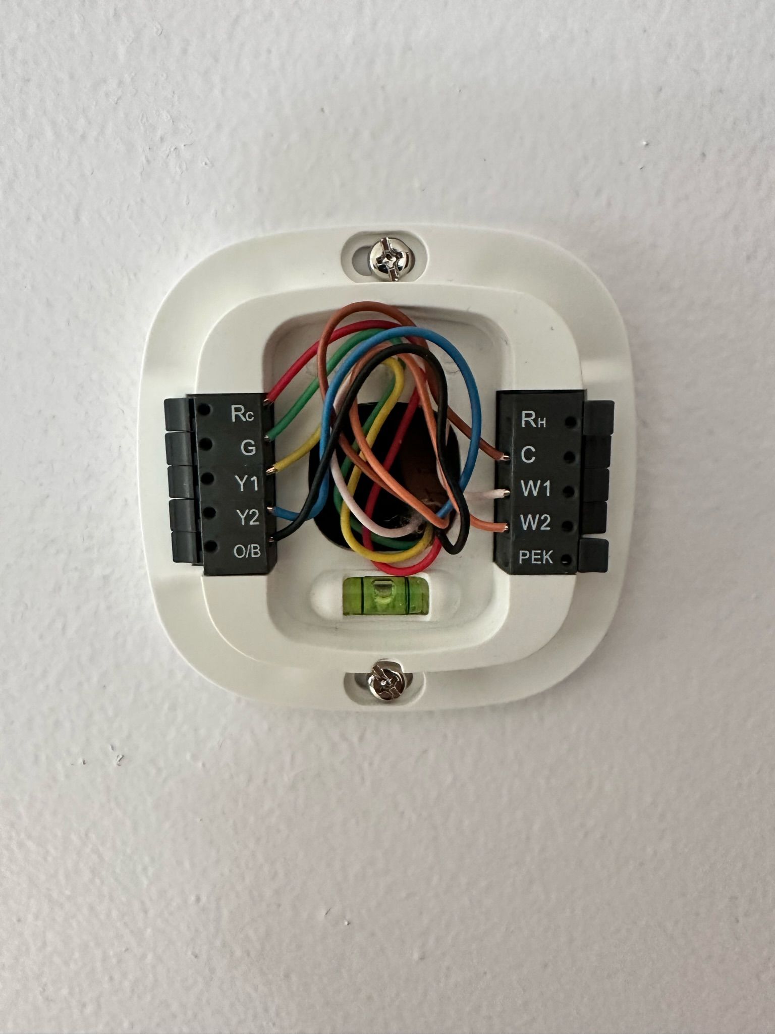 White wall-mounted thermostat base with colored wires connected to numbered terminals.