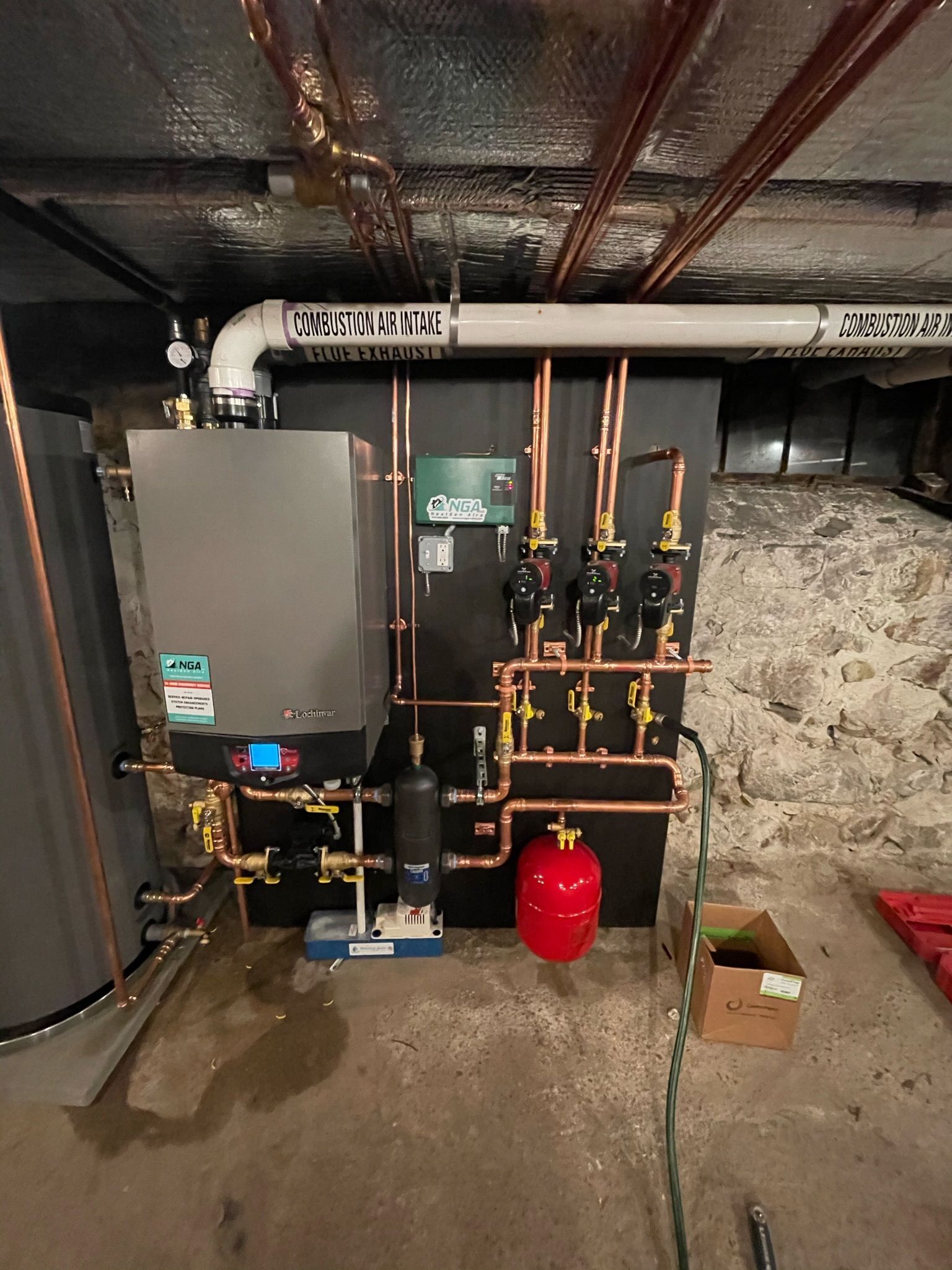 Heating system with copper pipes, a boiler, and a red expansion tank in a basement.