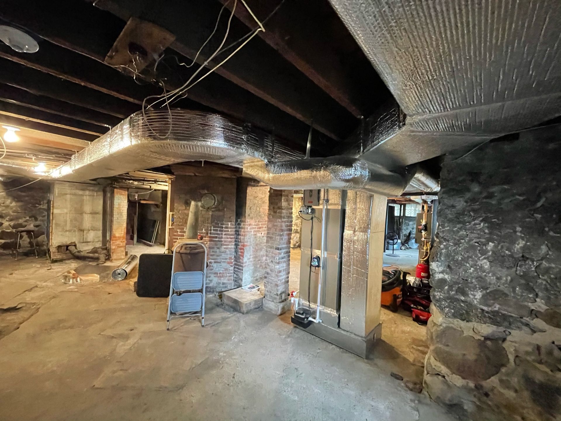 Basement interior with exposed beams, brick and stone pillars, and concrete floor.