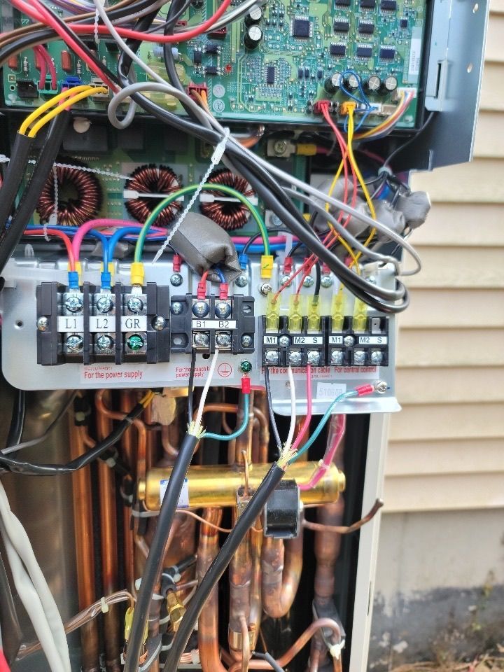Open view of electrical components within a heat pump unit, including wiring, relays, and copper tubing.