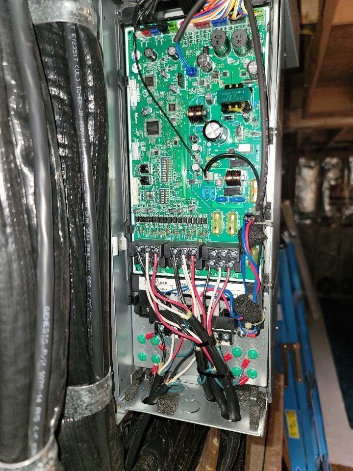 Open metal electrical panel with circuit board, wiring, and black insulated cables.