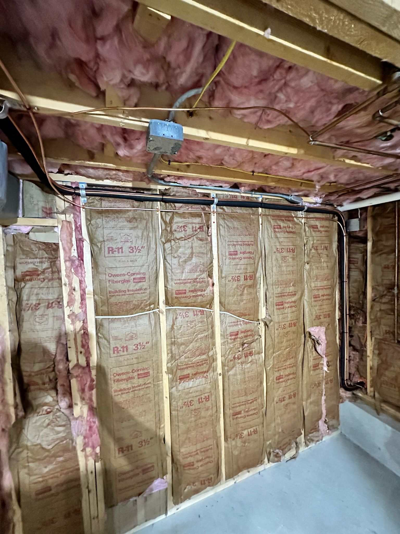 Basement wall with exposed insulation and electrical wiring, showing construction or damage.