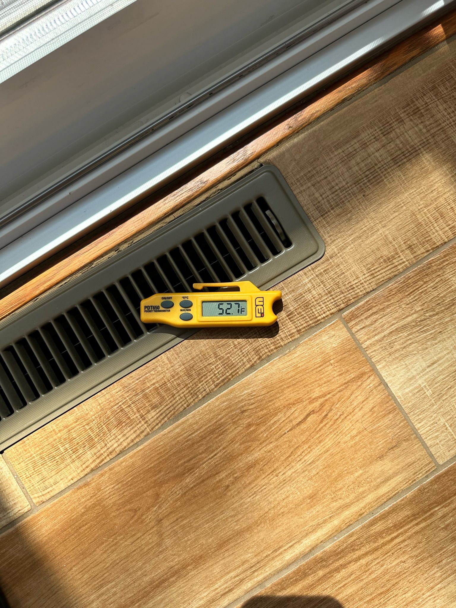 Yellow thermometer on a floor vent, showing a temperature of 72 degrees, in a room with wood-look flooring.