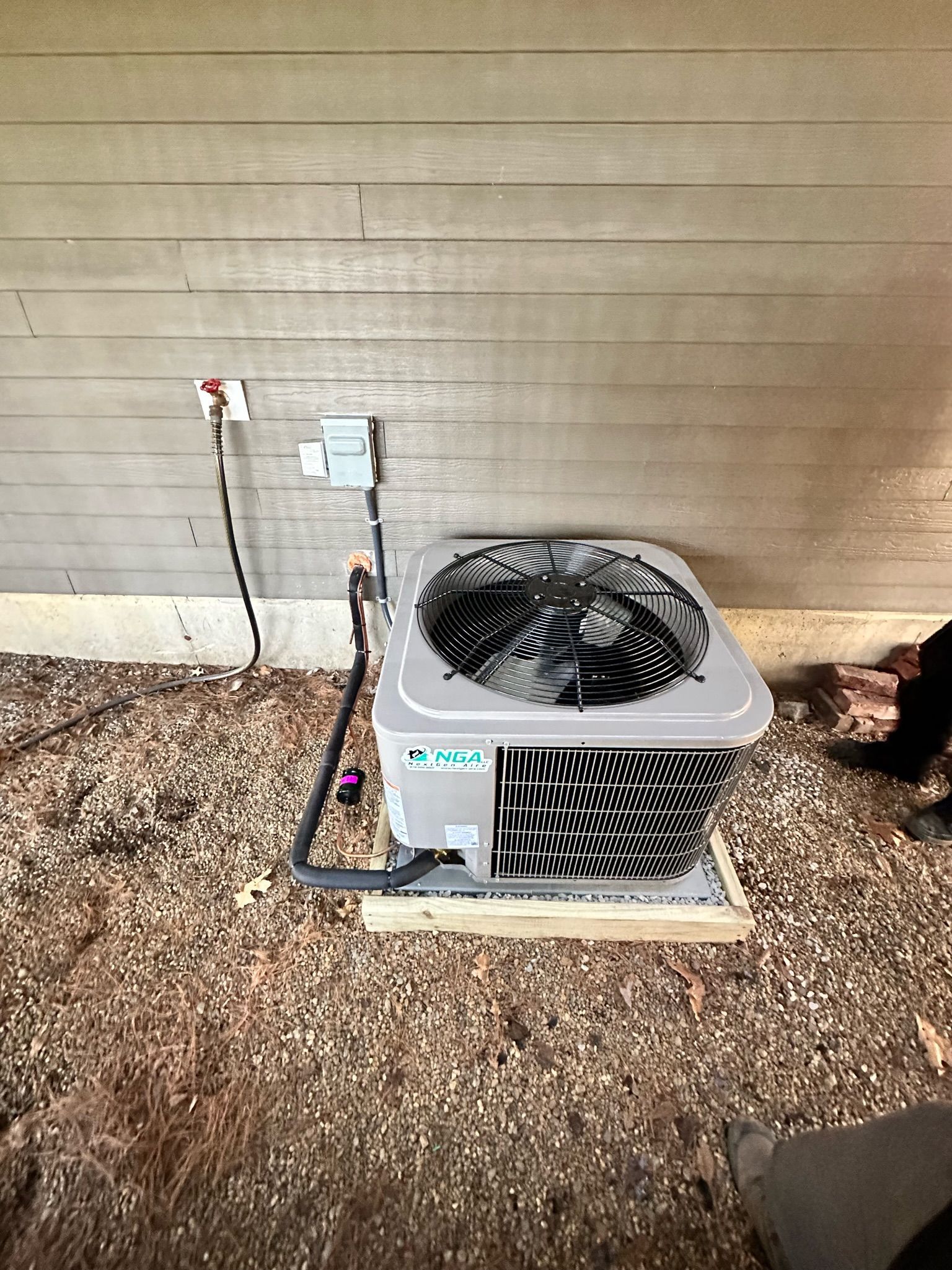 Air conditioning unit on a wooden base next to a tan building with electrical wiring.