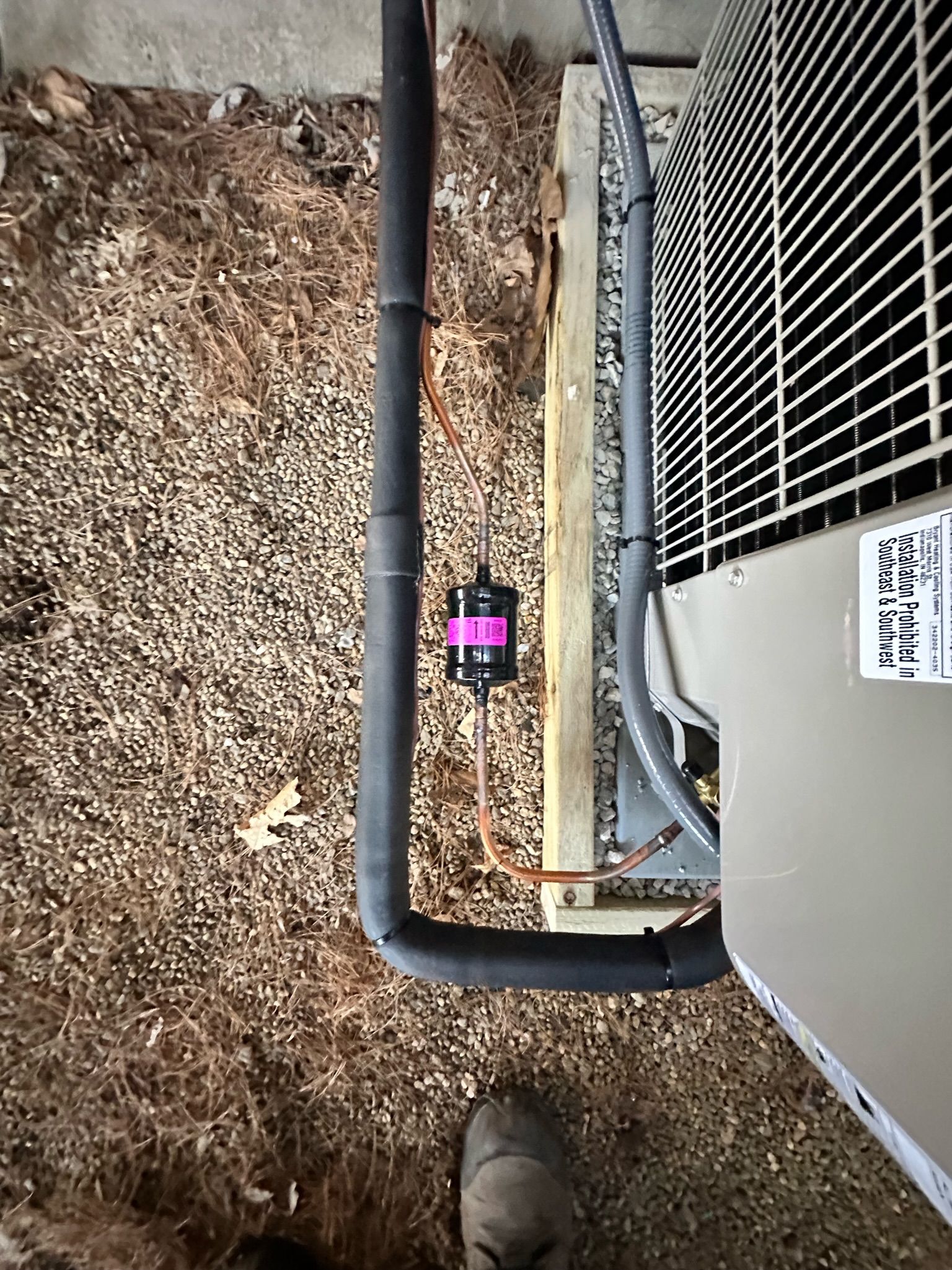 An air conditioning unit with black and copper pipes, and a pink filter.
