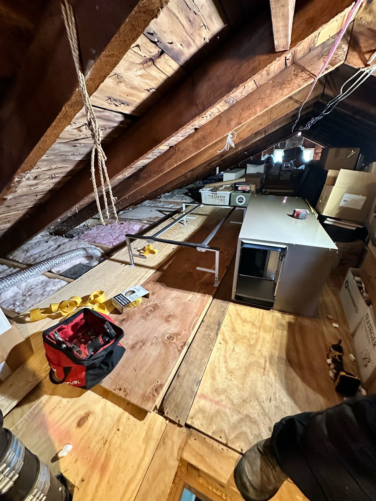Attic interior with plywood flooring, wooden beams, various boxes, and a red toolbox.