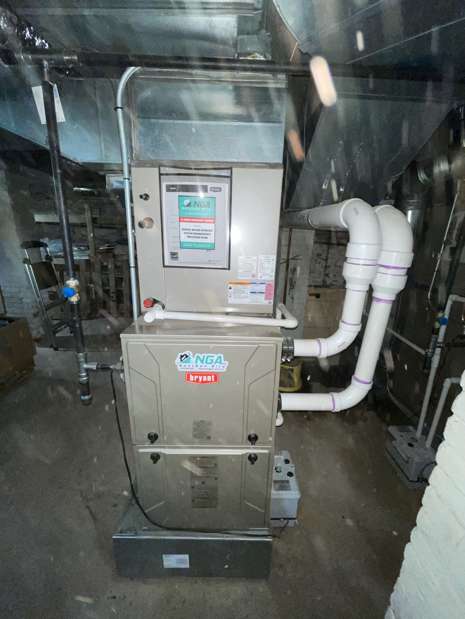 Furnace unit in a basement, with silver metal and white PVC pipes attached.