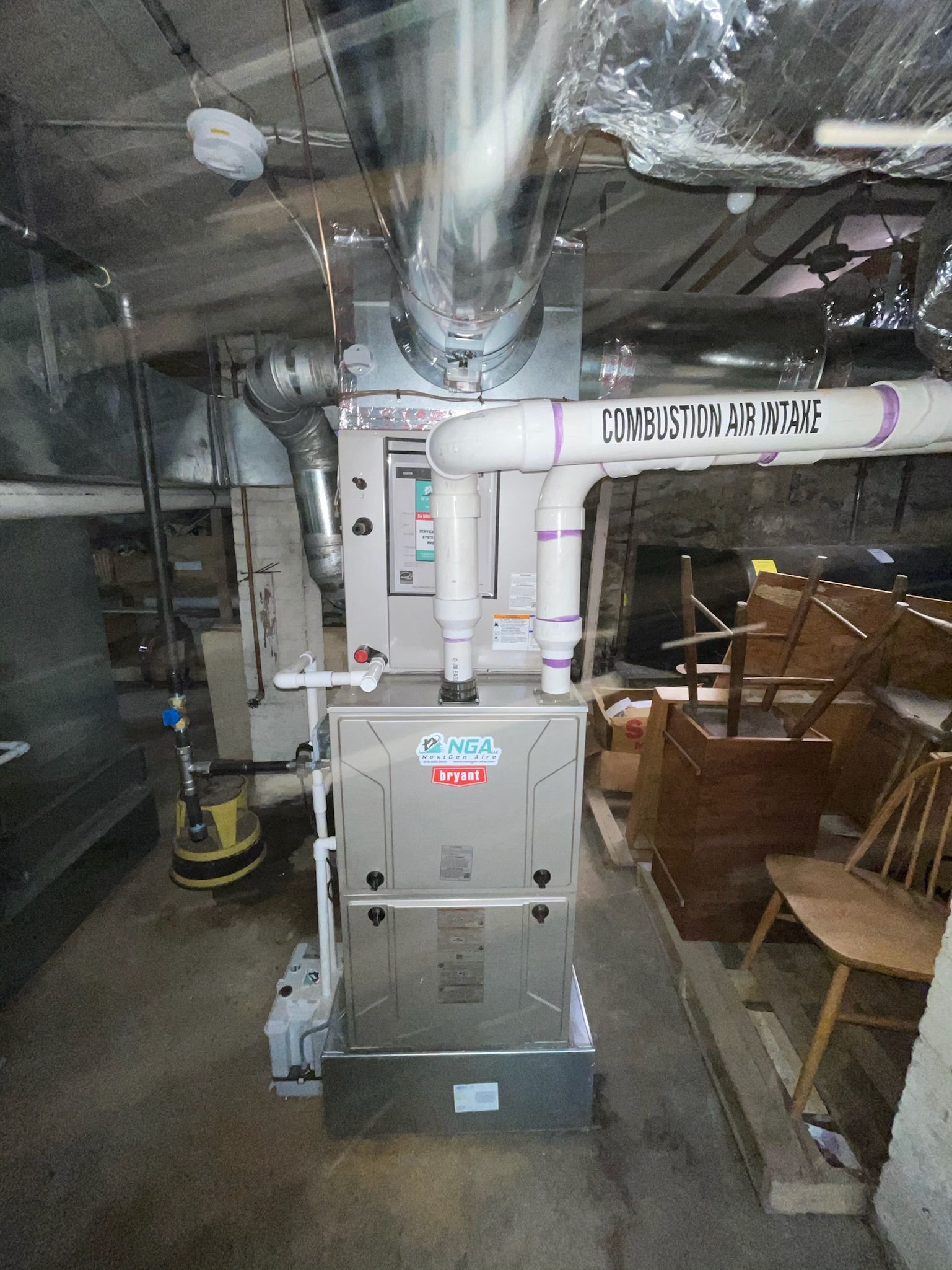 Furnace in basement with ductwork and pipes, near a sump pump.
