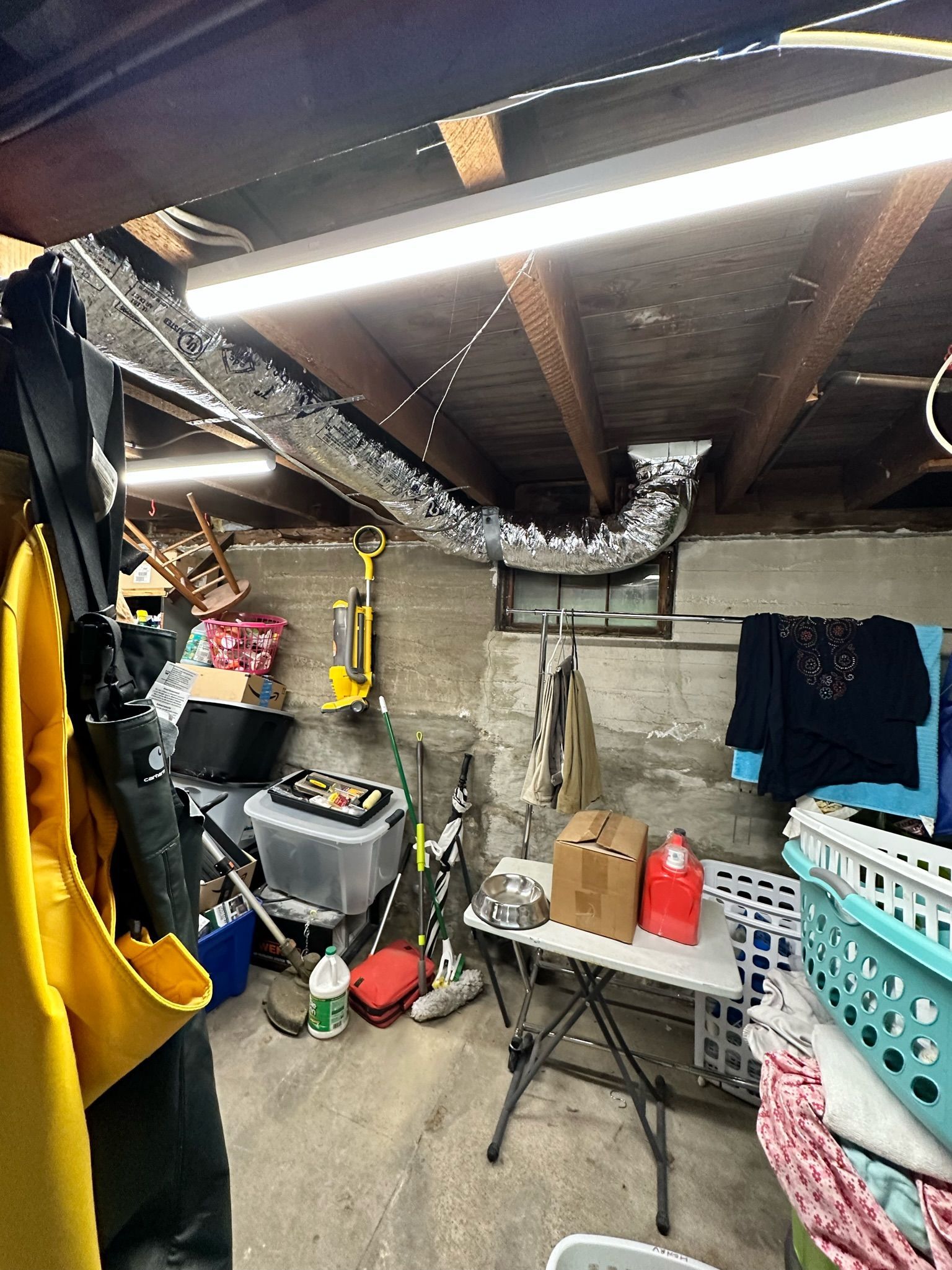 Cluttered basement with ductwork, concrete walls, storage, and laundry.