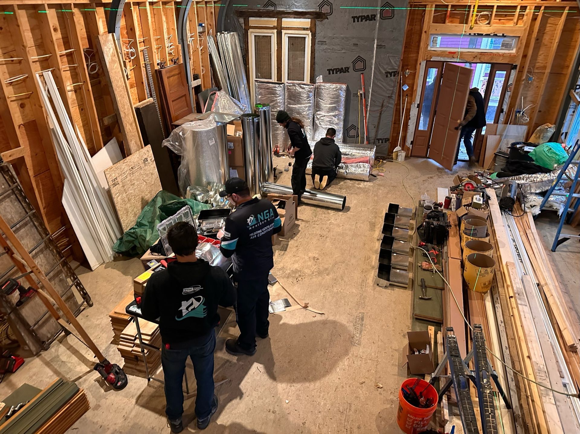 Construction workers inside a building under renovation. Wooden framing, materials, and insulation are visible.