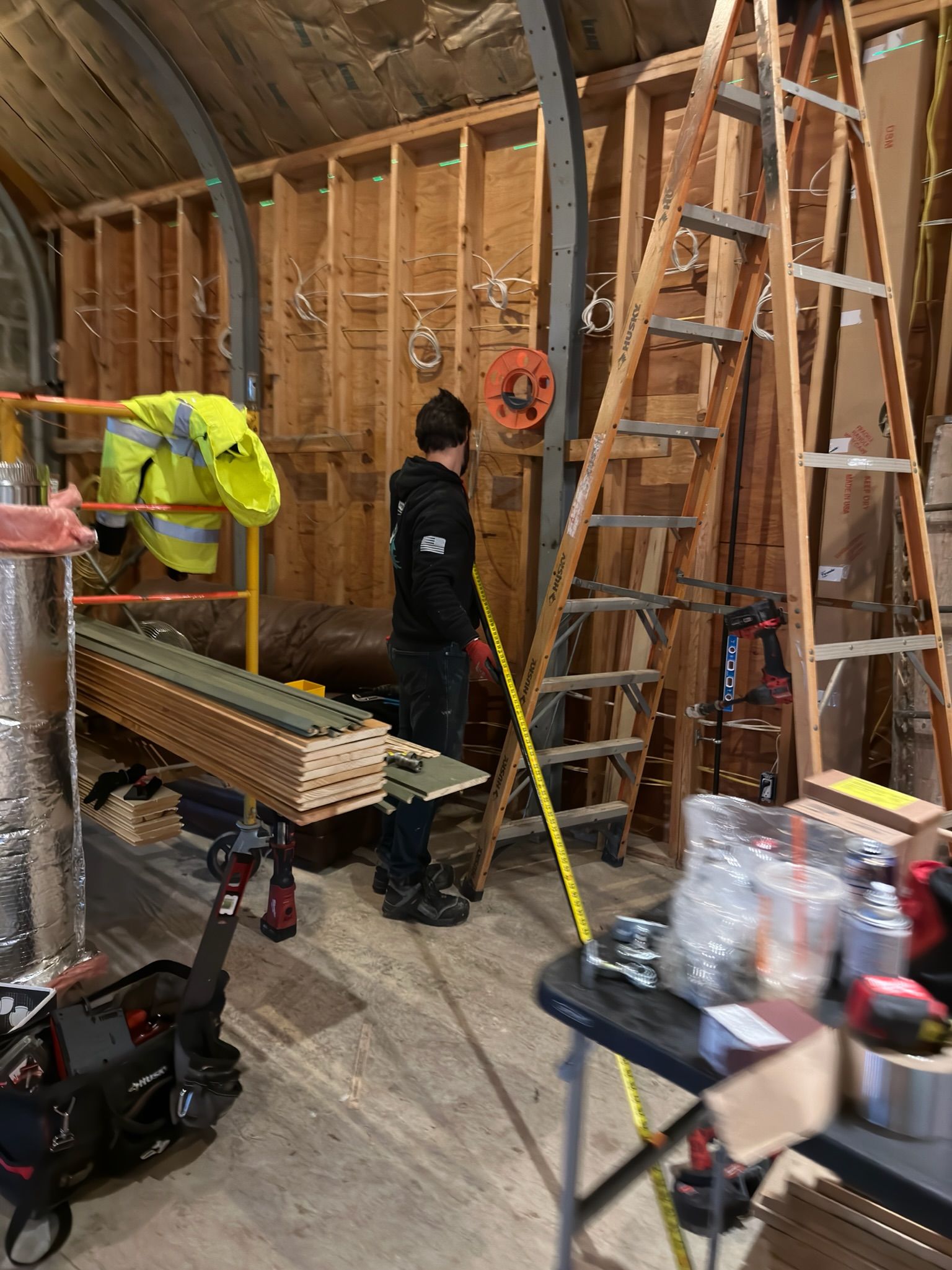 Person working in a construction area, wooden framing, ladder, tools, and materials.