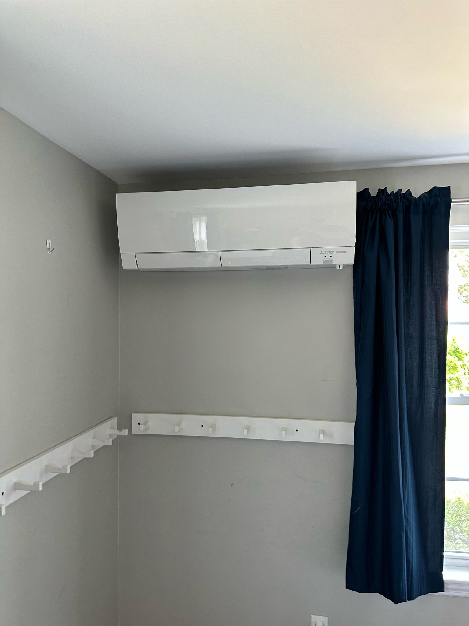 White air conditioner on a gray wall, blue curtain to the right. White shelf brackets are below.
