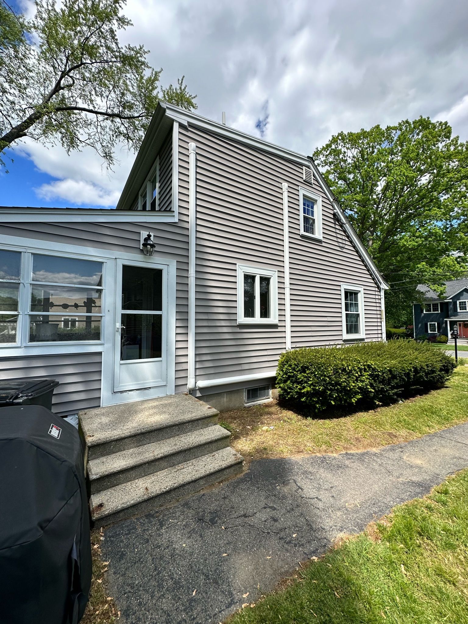 Gray shingled house with white trim and steps, small bush and path on the right.