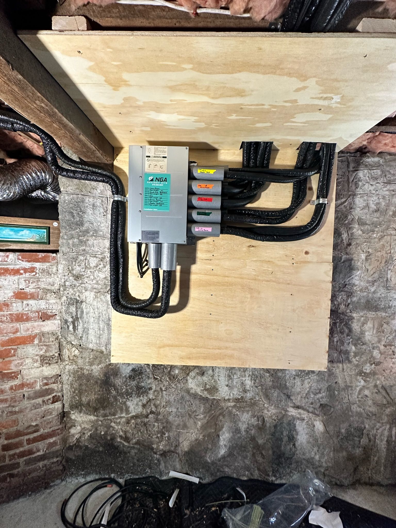 Electrical panel mounted on plywood in a basement, with black cables running to it.