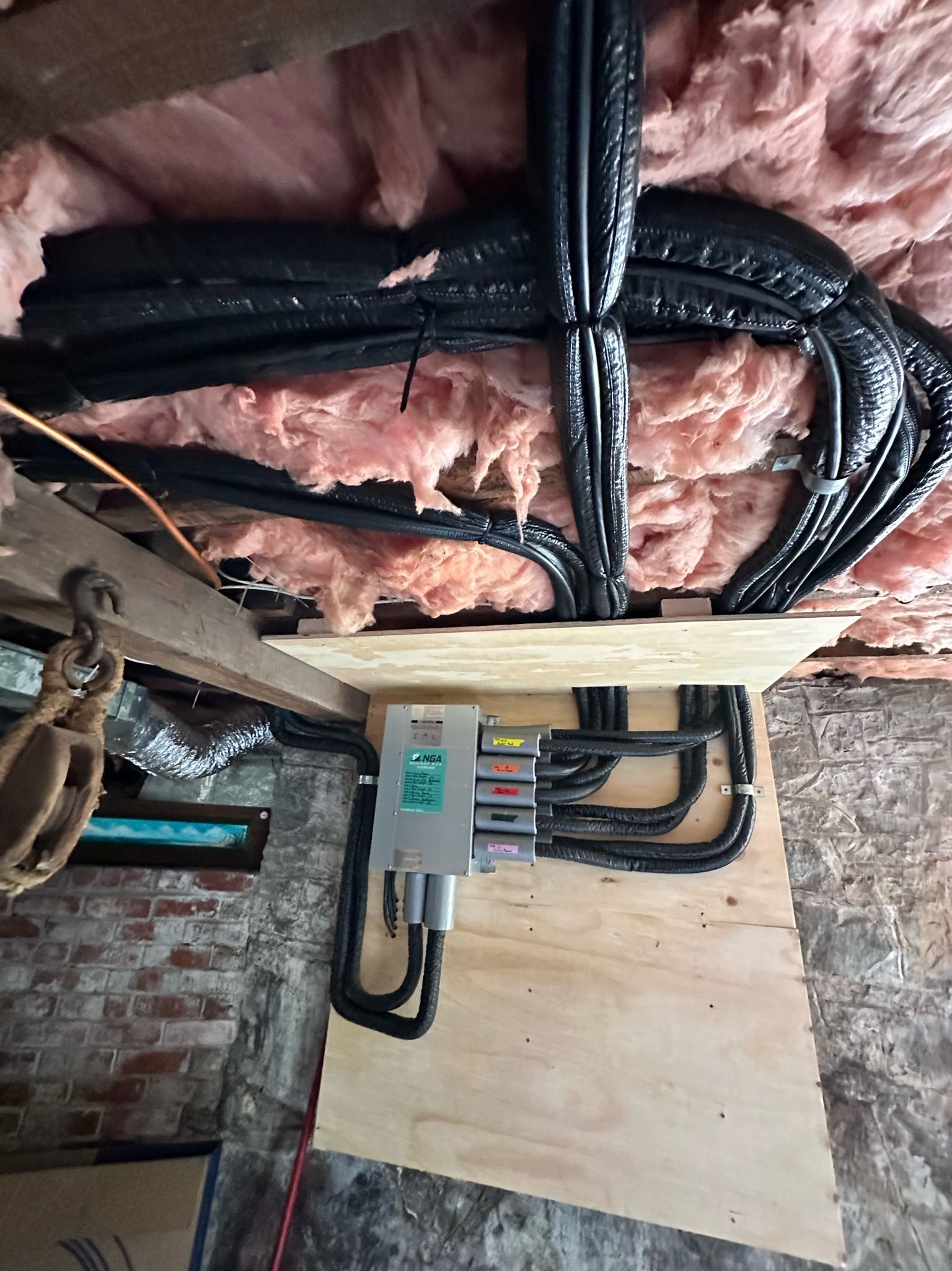 Electrical junction box with cables, wooden board, pink insulation, exposed brick wall.