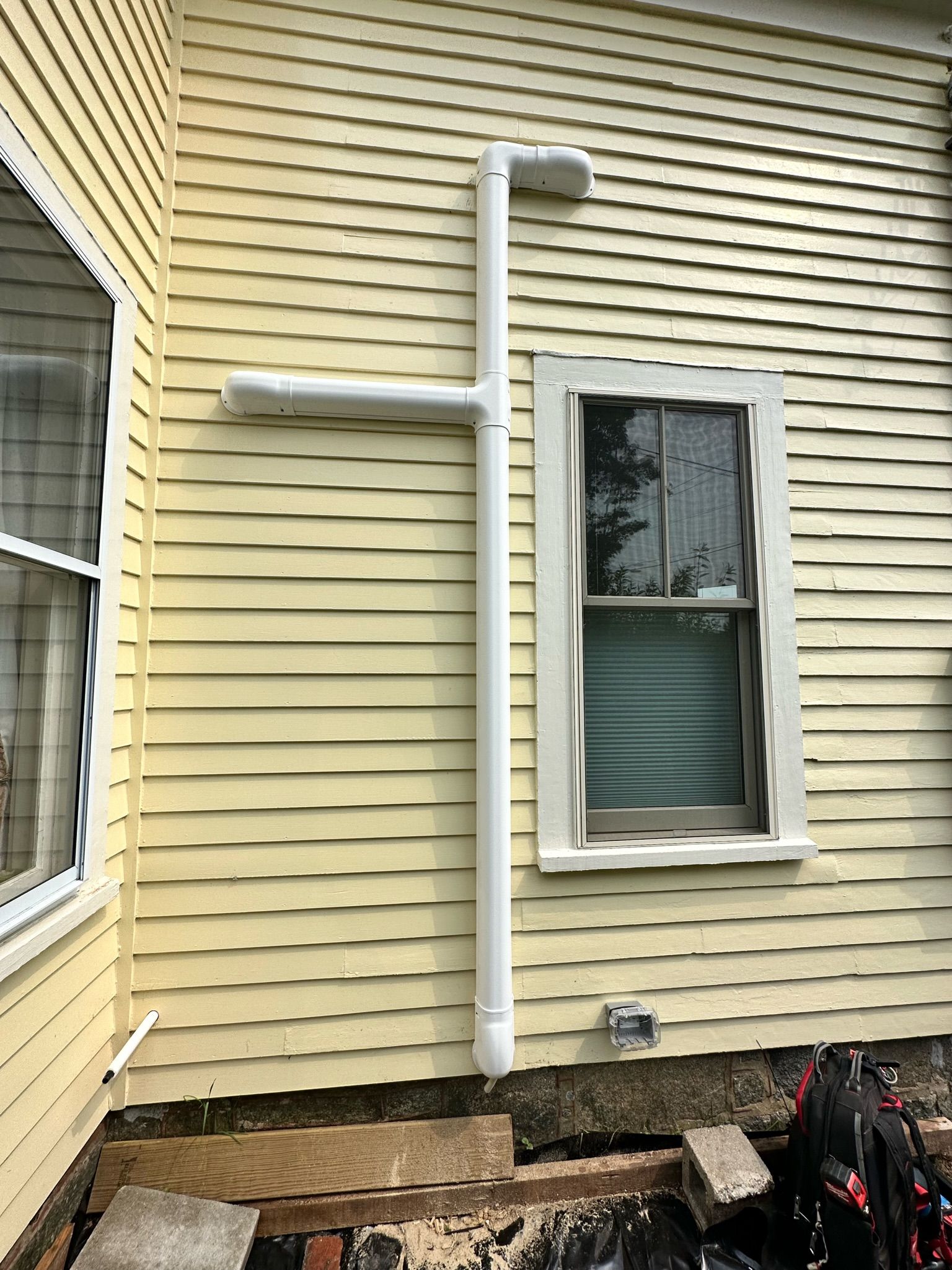 White pipes attached to yellow house siding, near window.