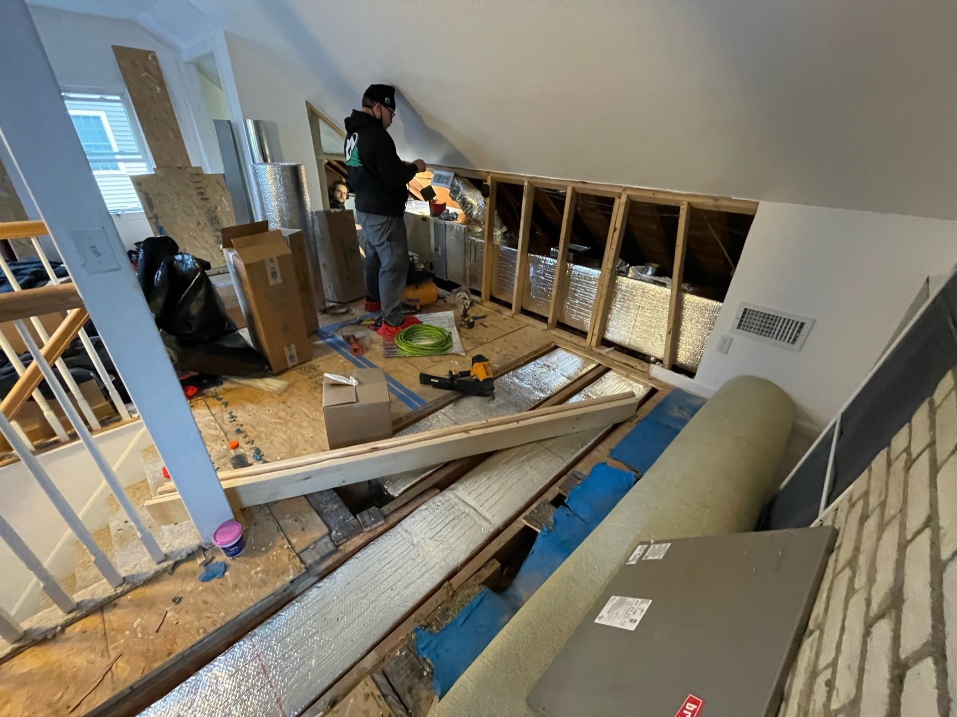 Person working on construction in an attic with insulation, wood beams, and various building materials.