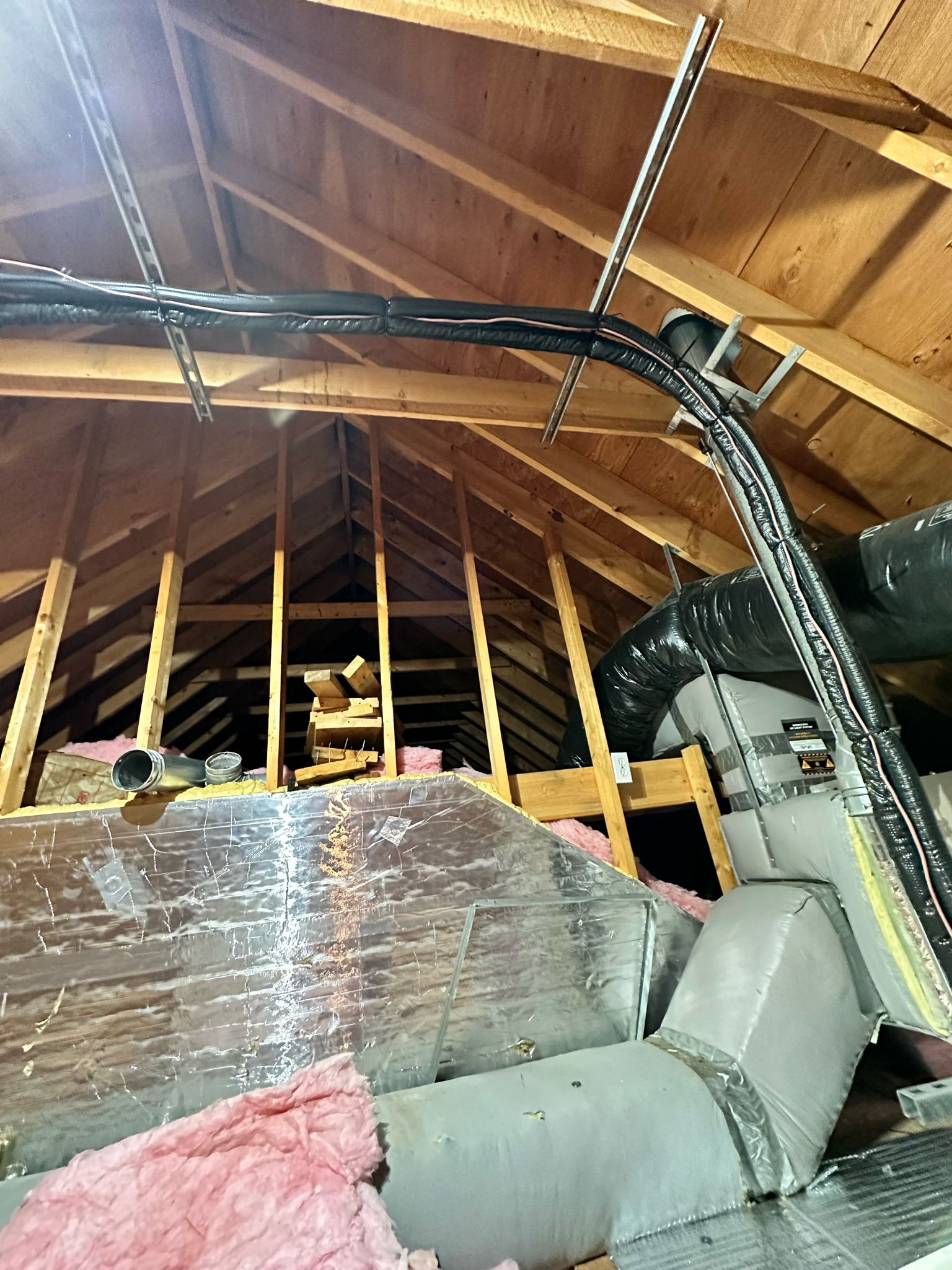 Attic with wooden beams, insulation, ductwork, and electrical wiring.
