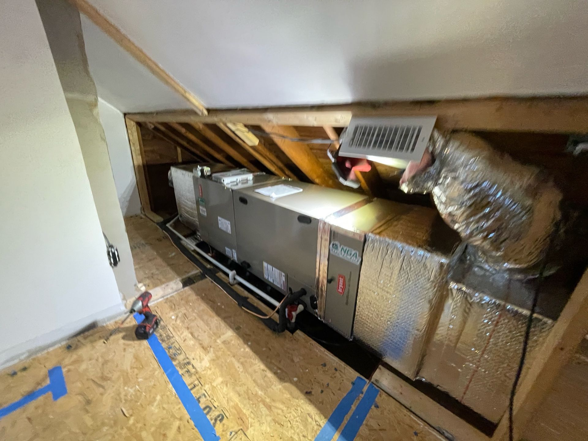 HVAC unit installed in an attic. Ductwork, vent, and tools are visible.