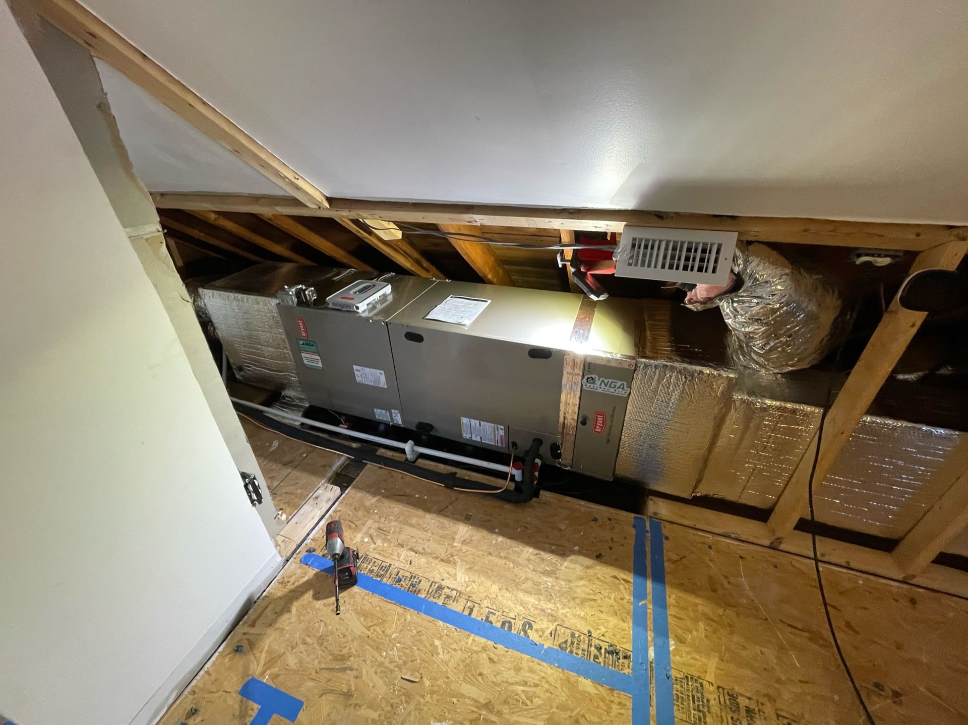 HVAC unit installed in an attic. Ductwork, electrical components, and wood framing are visible.