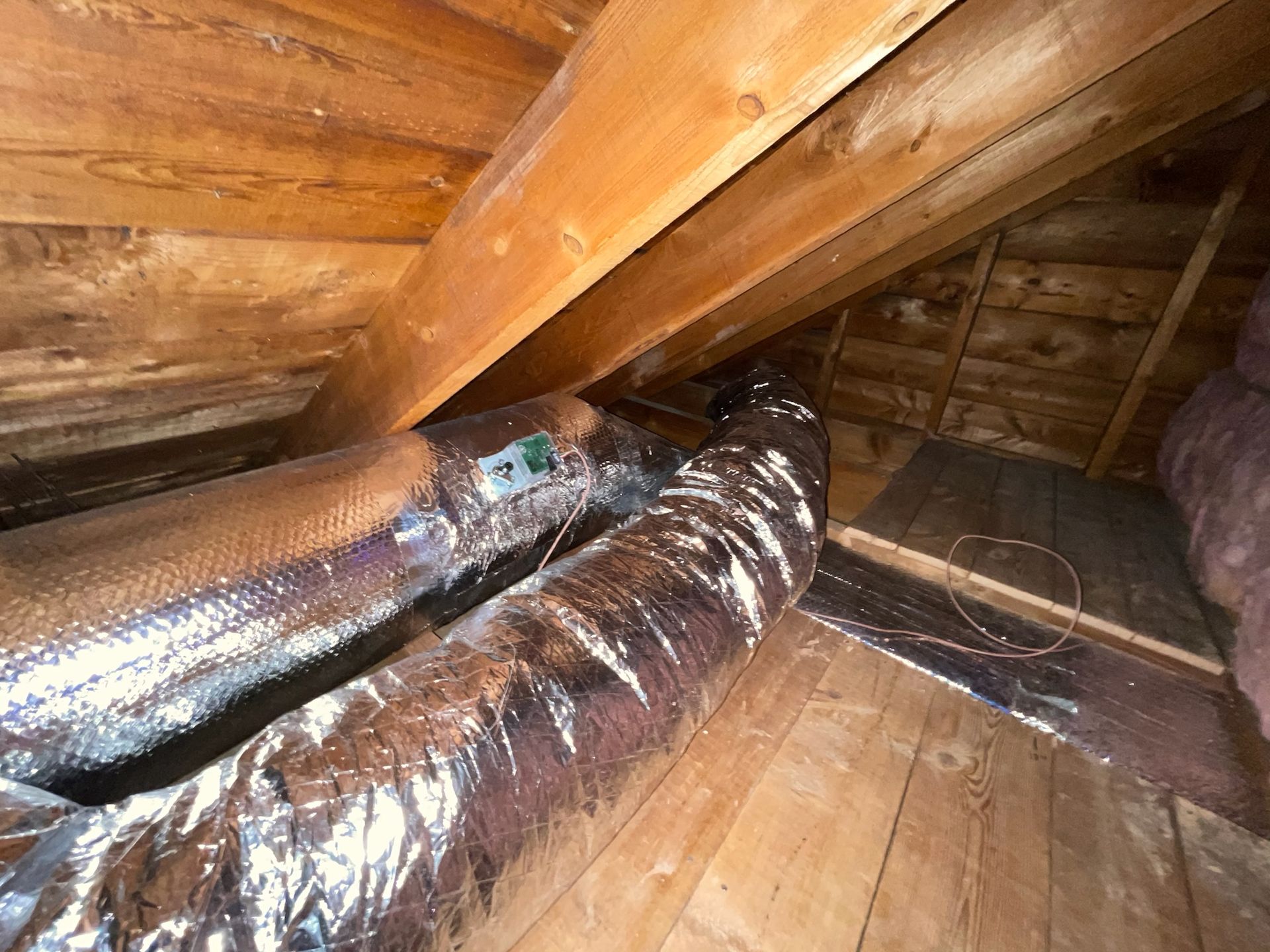 Attic interior with wooden beams, insulated air ducts, and exposed wooden walls.
