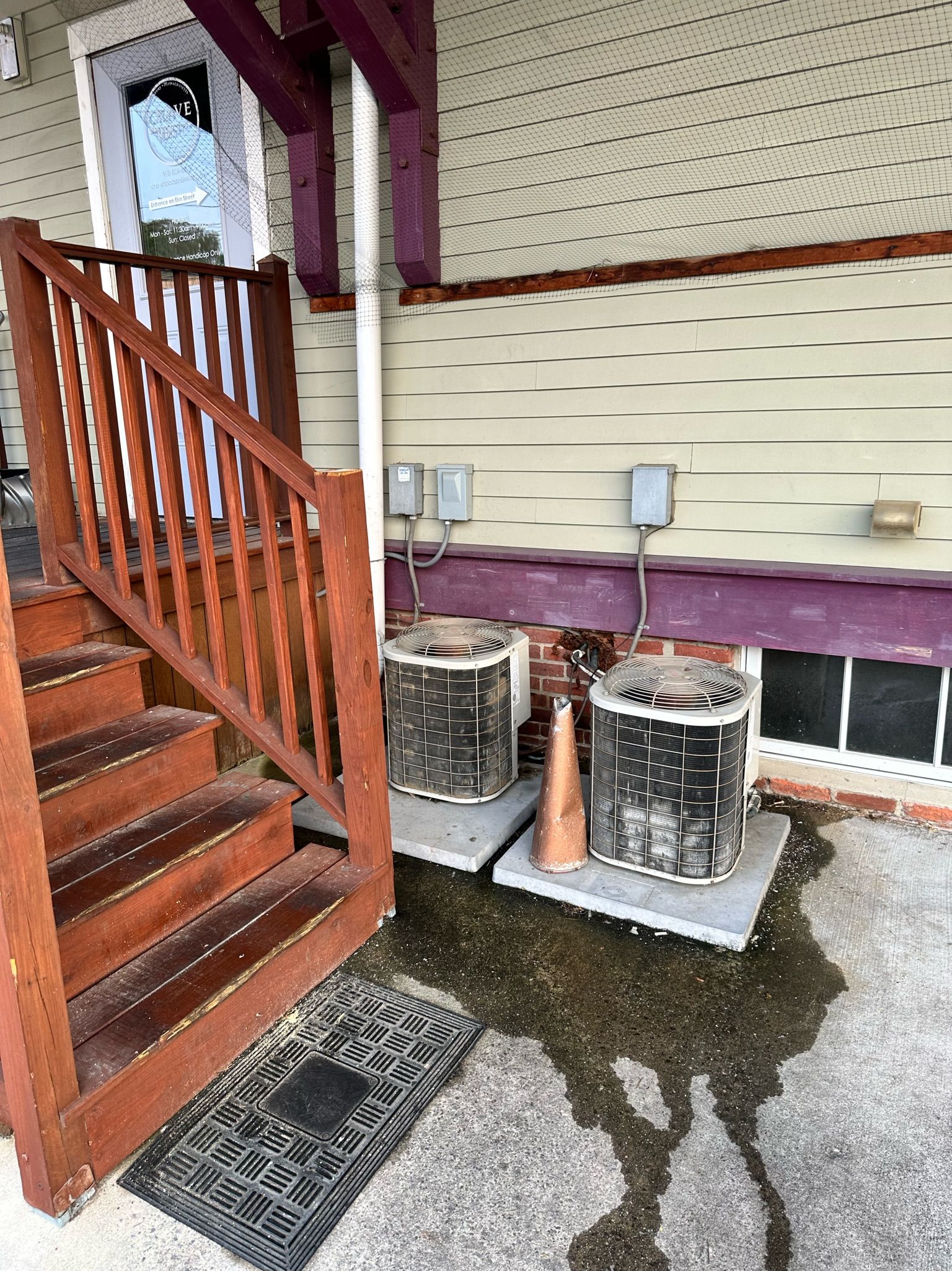 Wooden steps lead to a porch with two AC units on concrete pads. Water puddles.