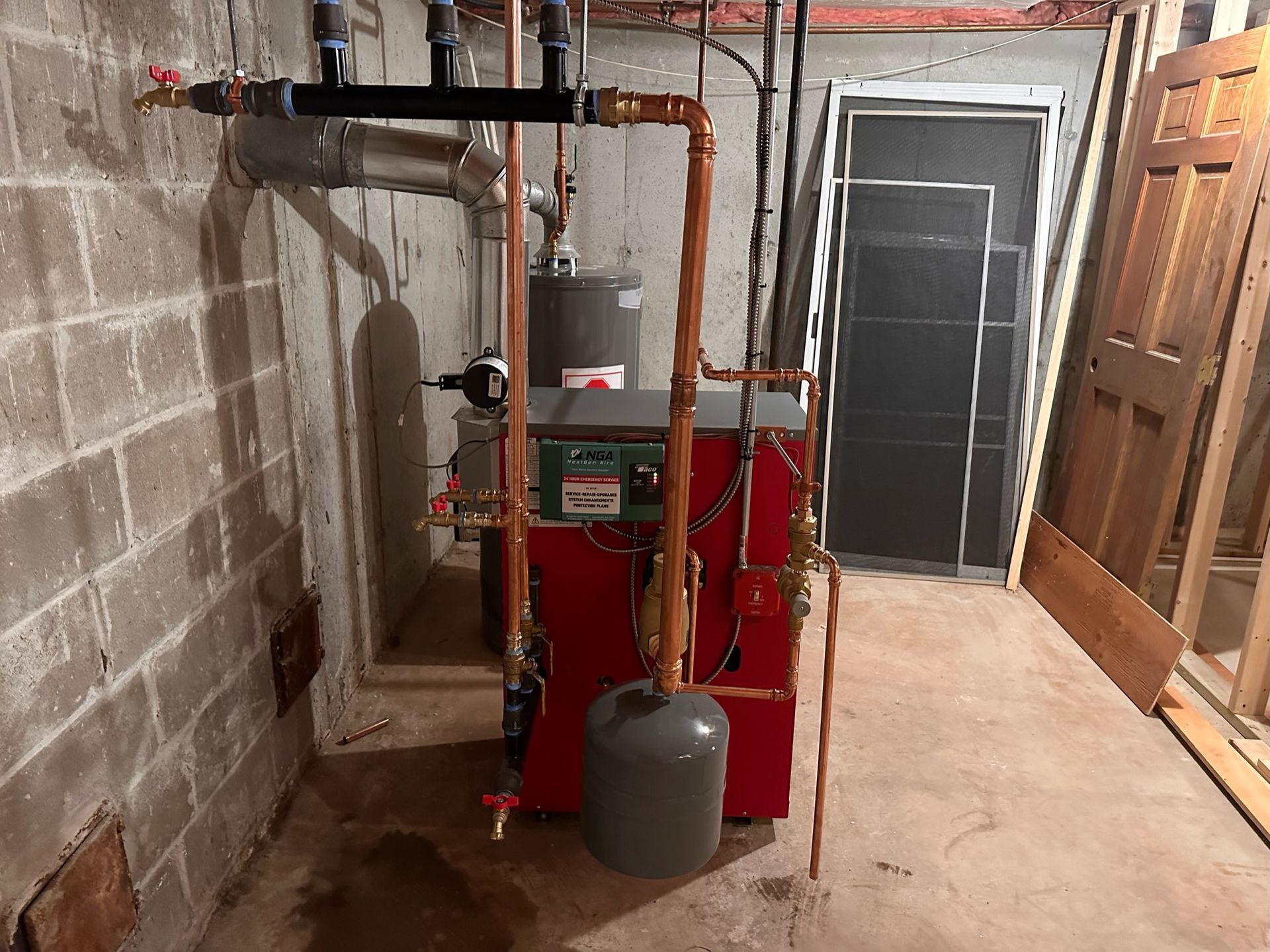 Red heating system with copper pipes in a basement against a concrete block wall.