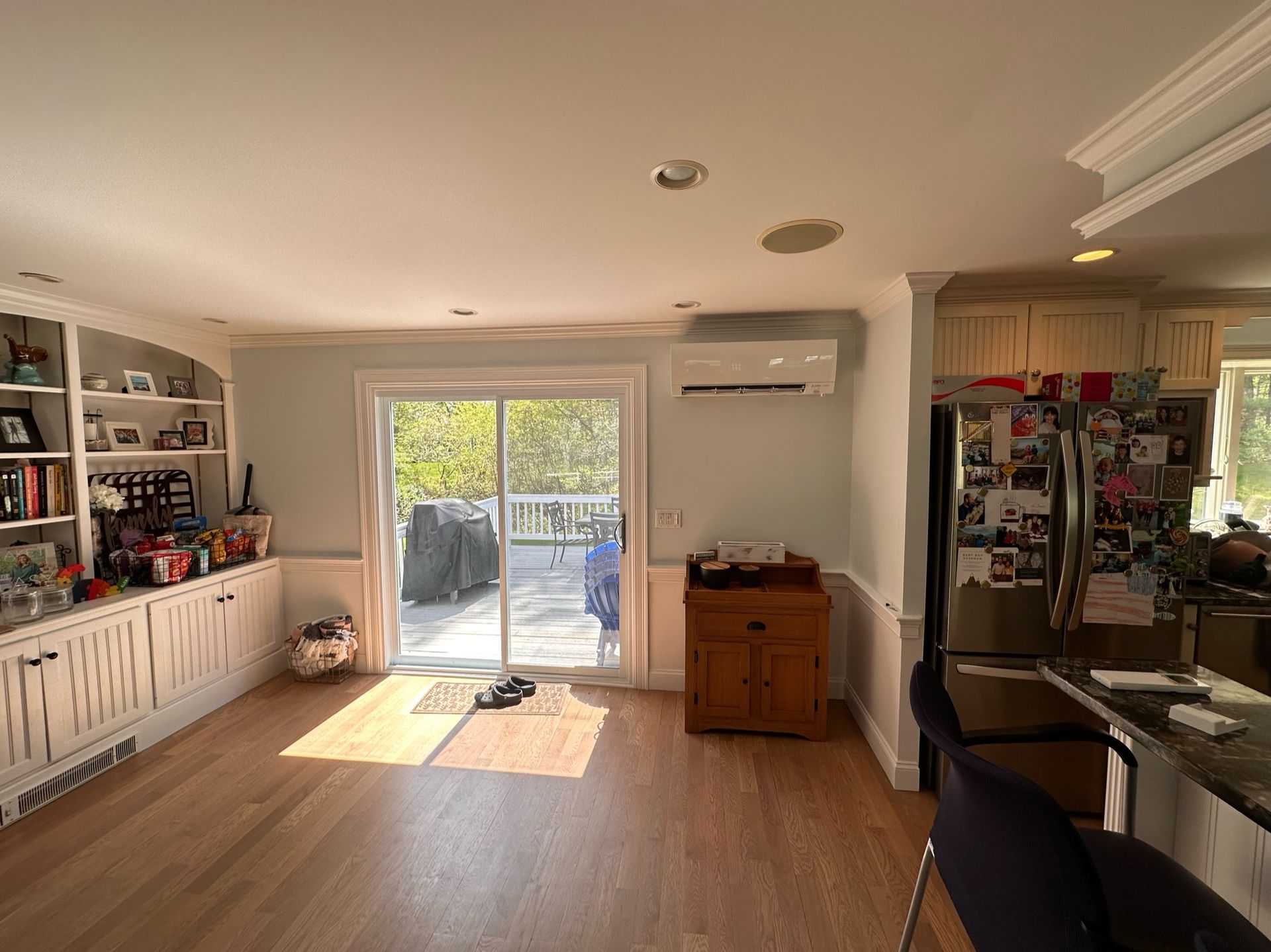 A sunny kitchen with light wood floors, built-in shelves, a sliding door to a deck, and an island with bar stools.