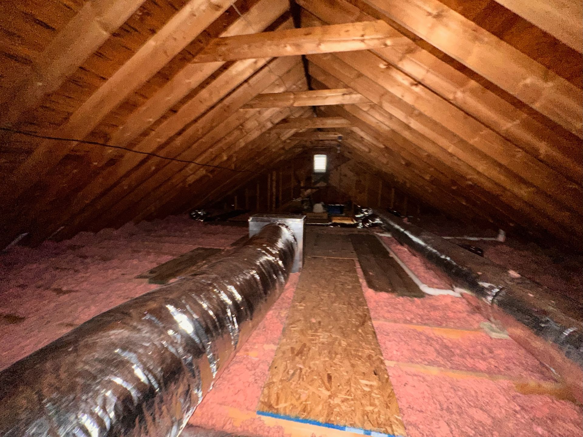 Attic interior with exposed wooden rafters, pink insulation, and a metal duct system.