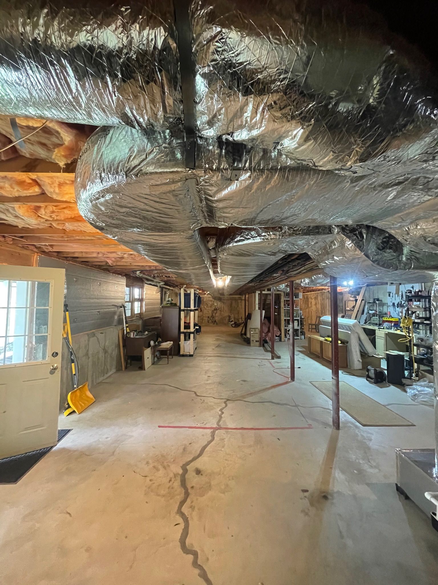 Basement with concrete floor, ductwork overhead, support beams, and tools along the right wall.