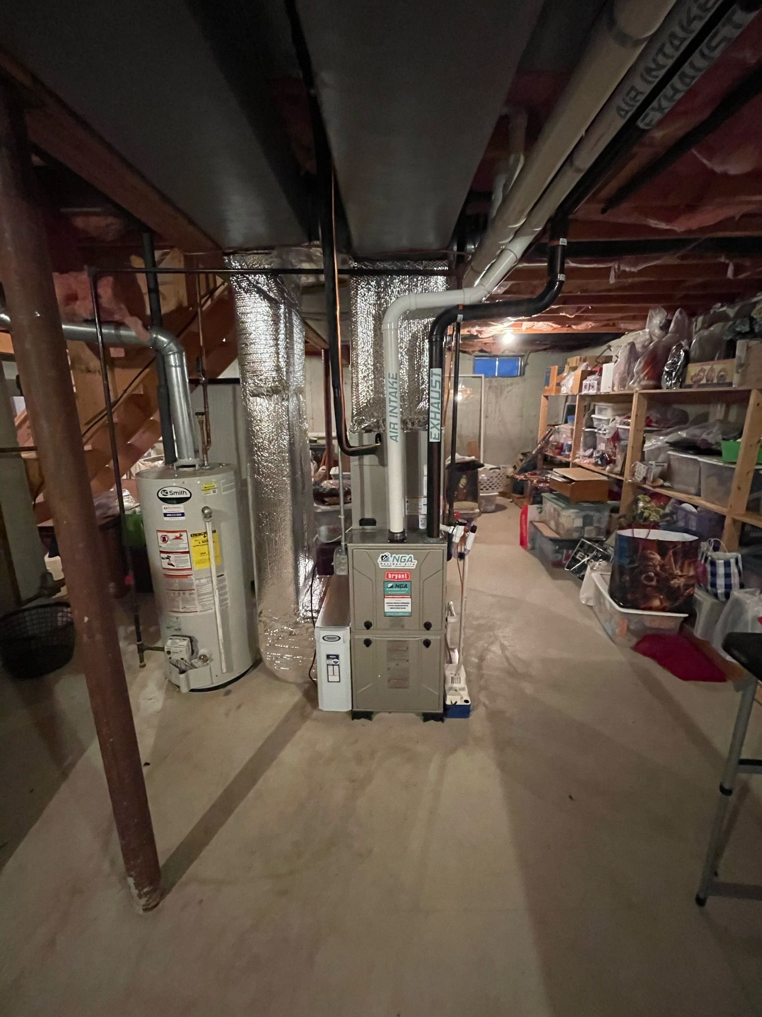 Basement with a furnace, water heater, ductwork, and shelving along a wall.
