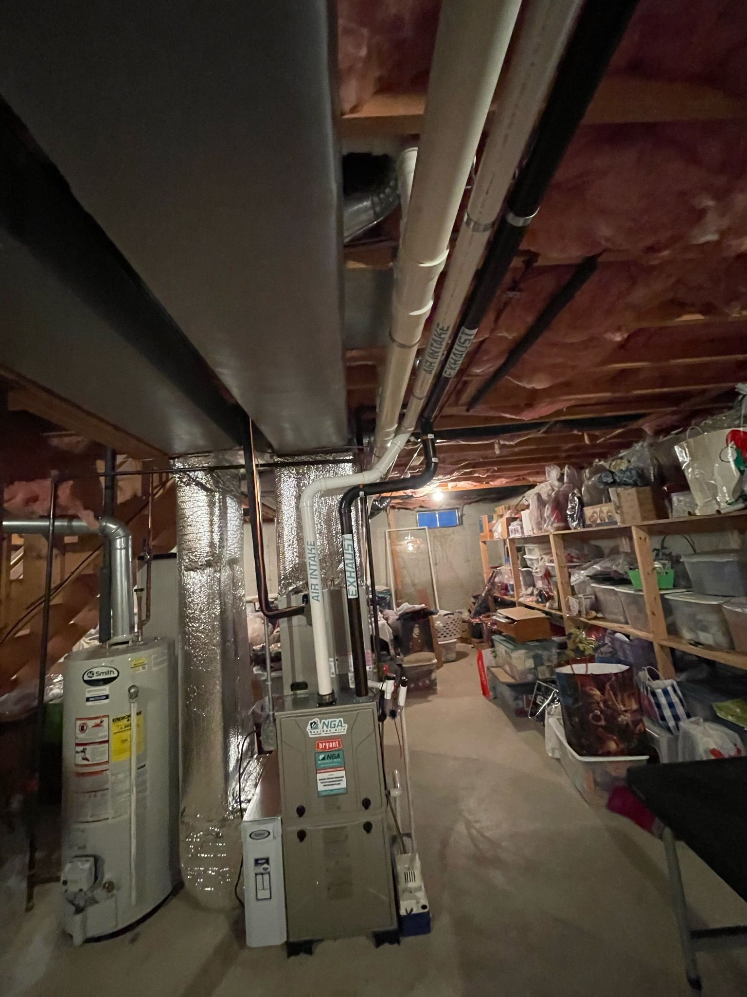 Basement with furnace, water heater, ductwork, and storage shelves along a narrow hallway.