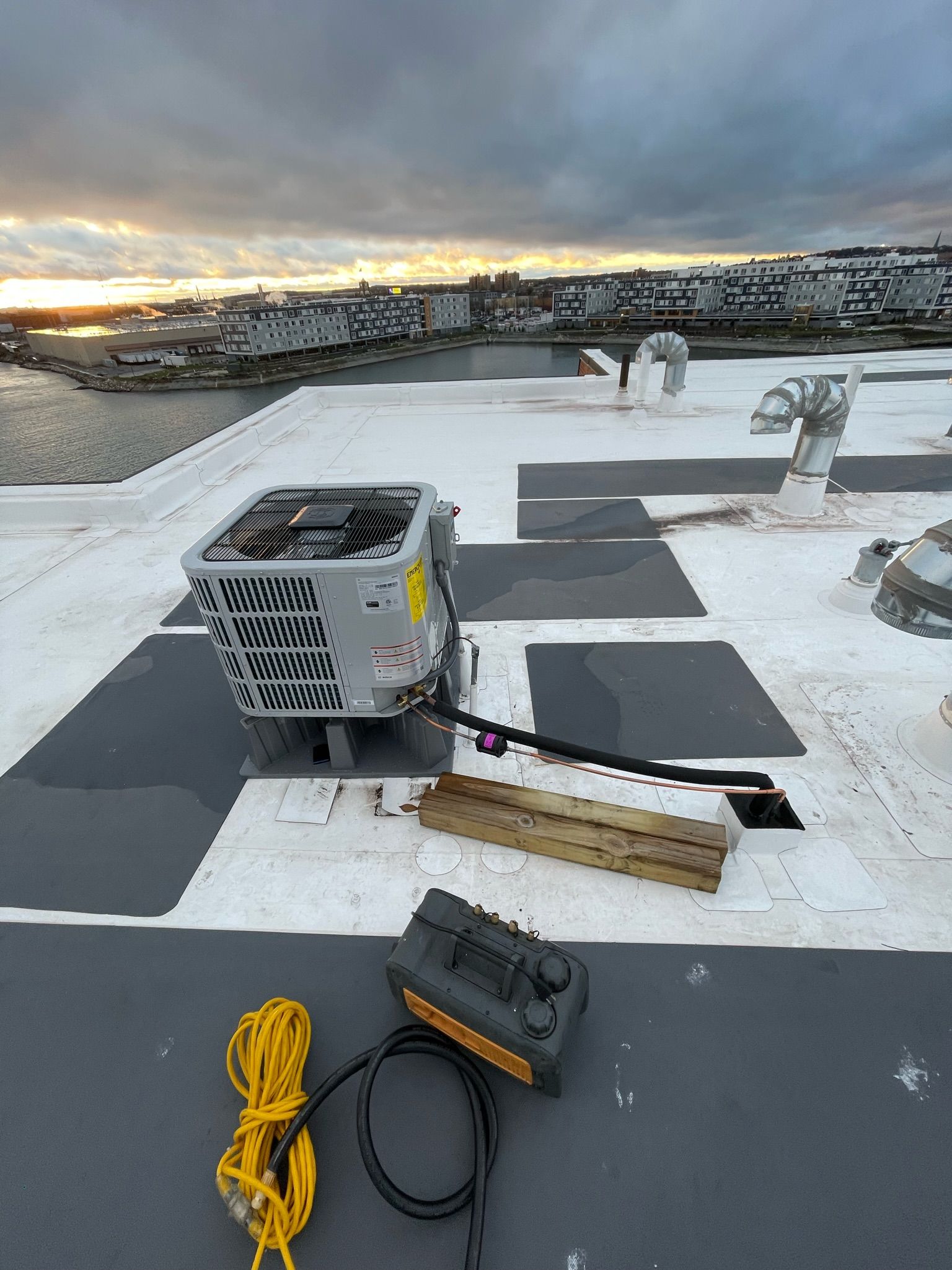 HVAC unit on a snowy rooftop with a waterfront view and power cord.