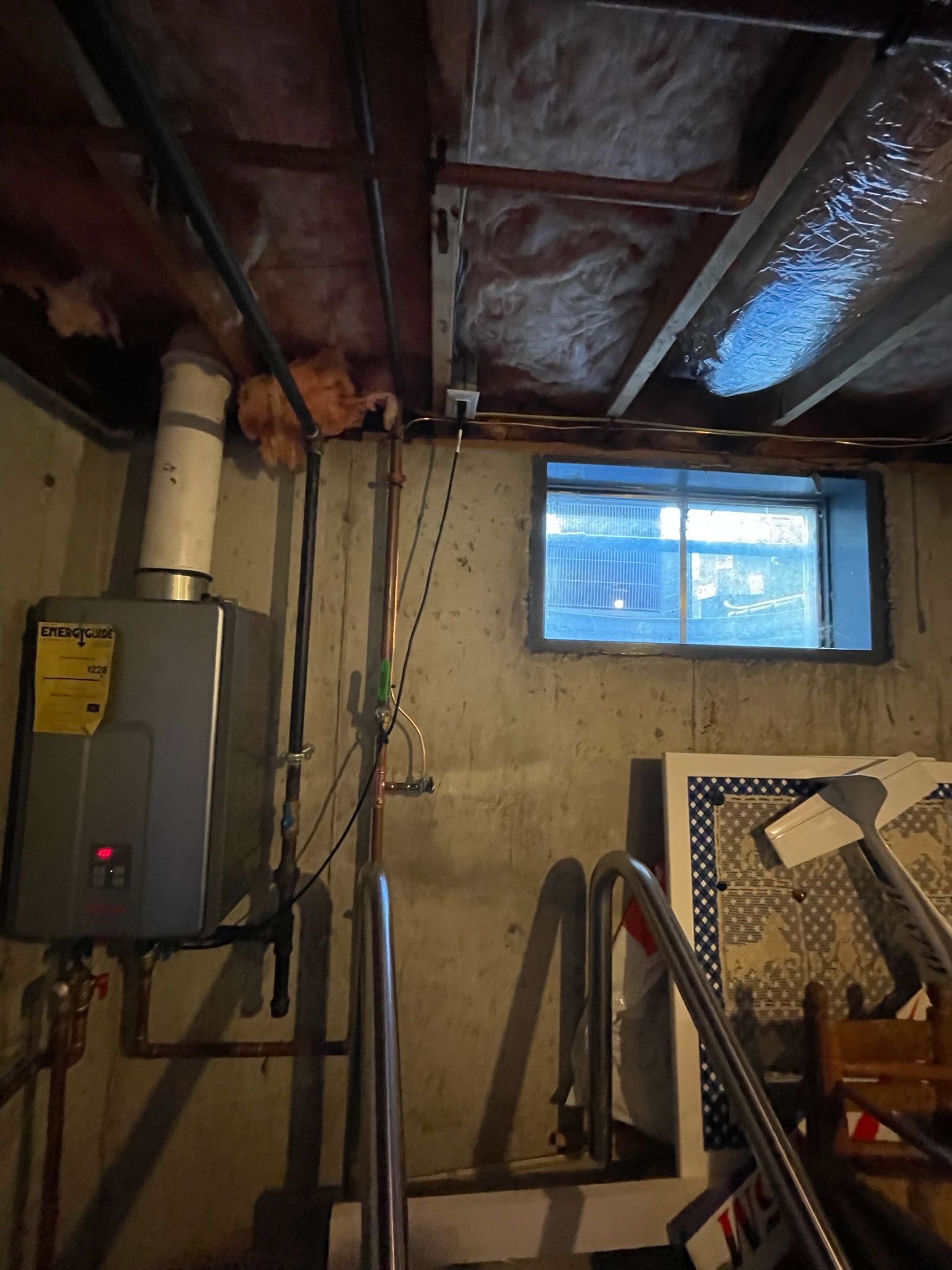 Basement with water heater, pipes, window, and stairs. Concrete walls, wood ceiling with insulation.