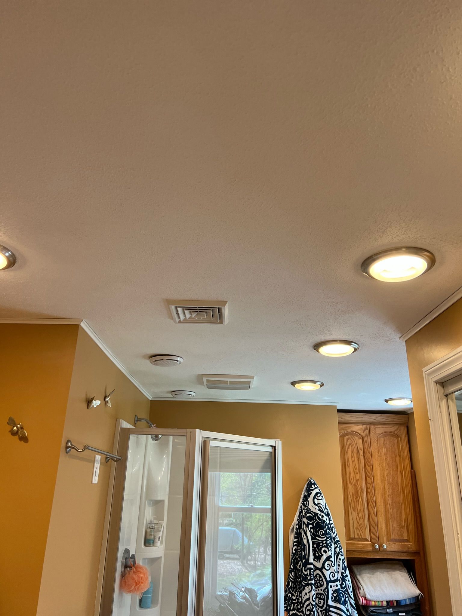 Yellow-walled hallway with recessed ceiling lights and a shower; a blue and white patterned towel hangs on the right.