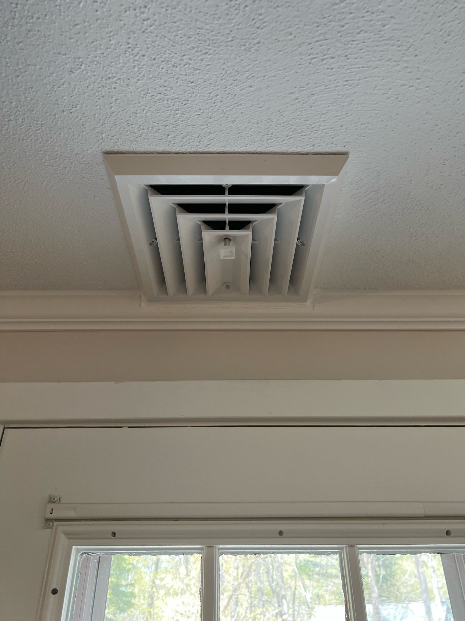 White ceiling vent on a textured ceiling, centered above a window.