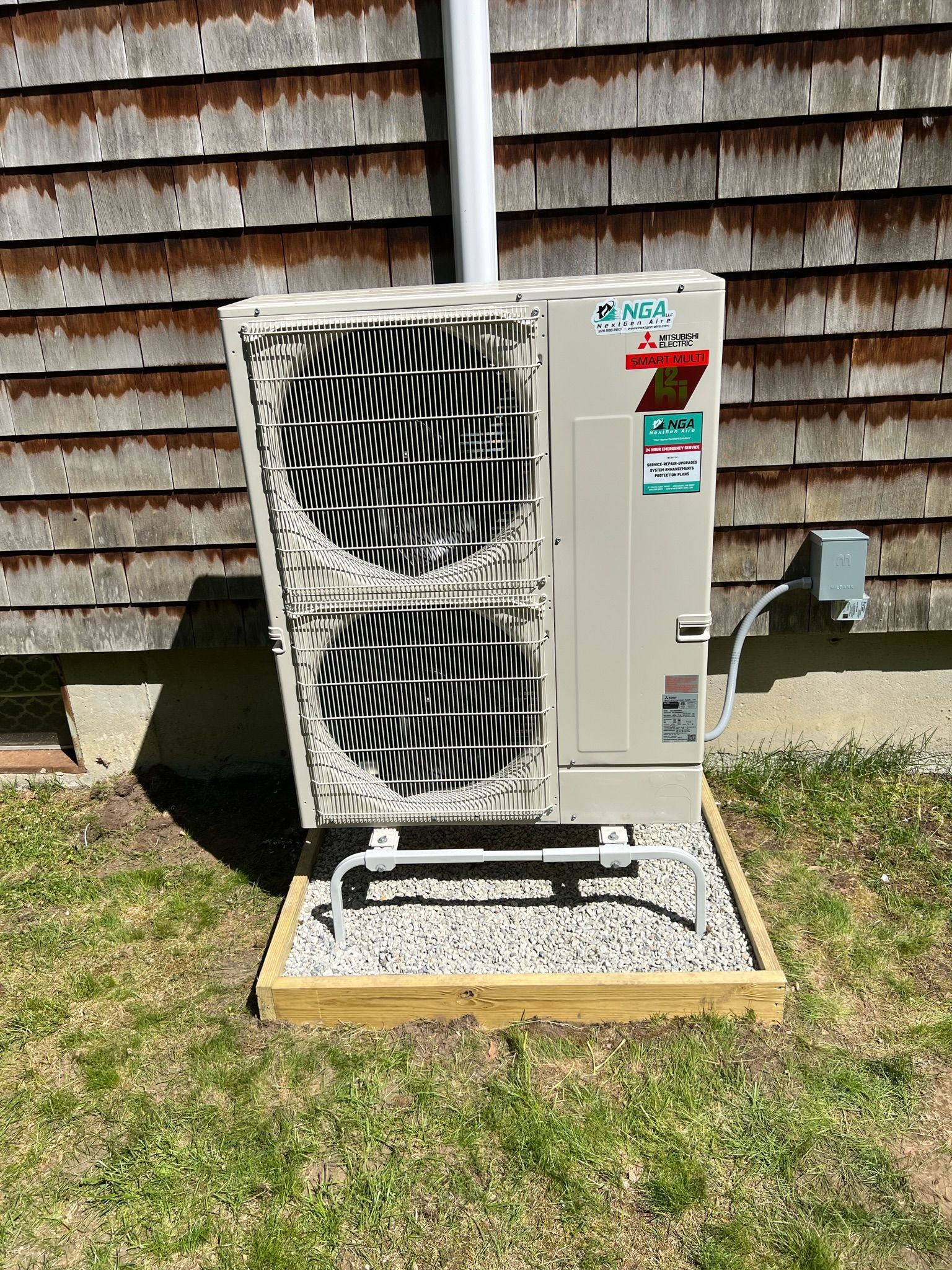 Heat pump unit on gravel base next to wood-shingled building, white and tan with a gray electrical box.