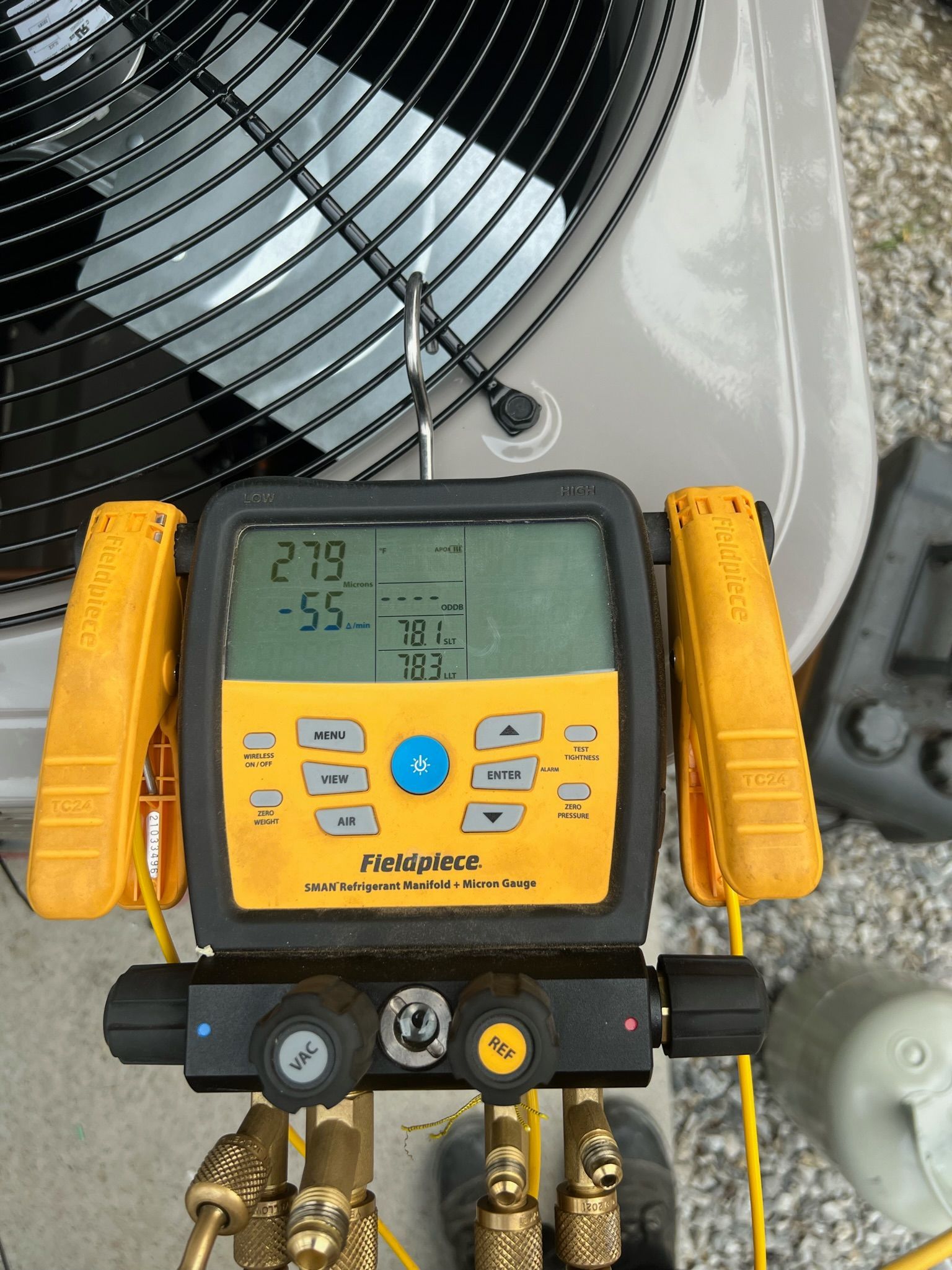 A yellow and black digital manifold gauge hooked up to an AC unit, displaying pressure readings.