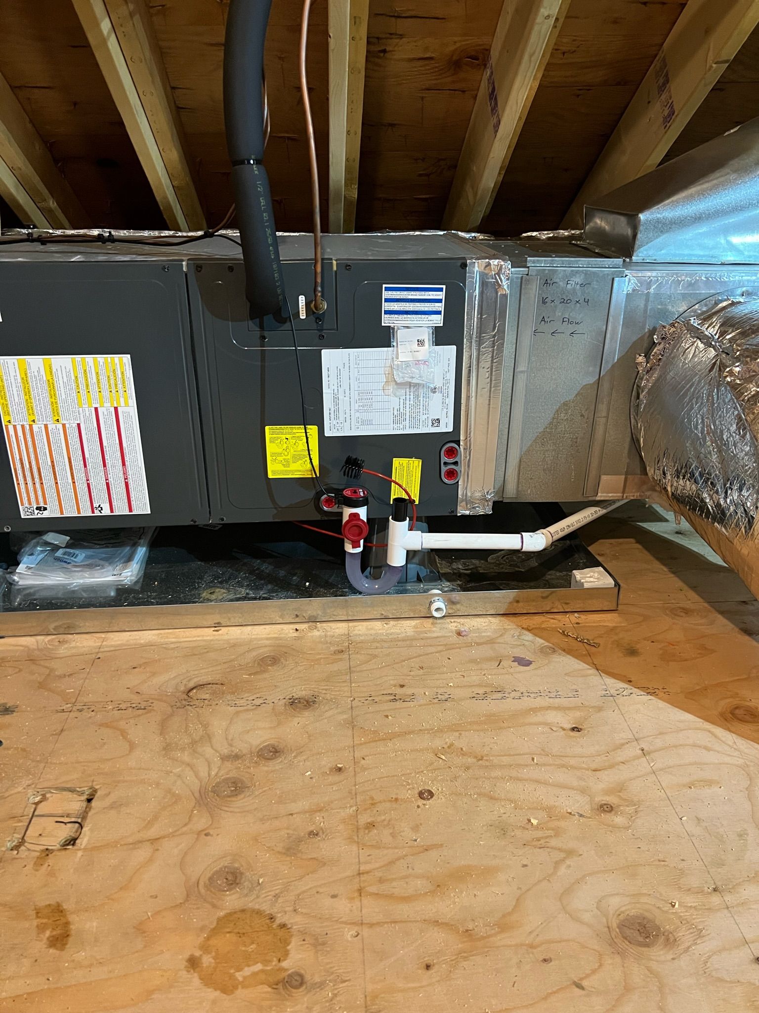 HVAC unit installed in a wooden attic, with ductwork and drainage pipes.