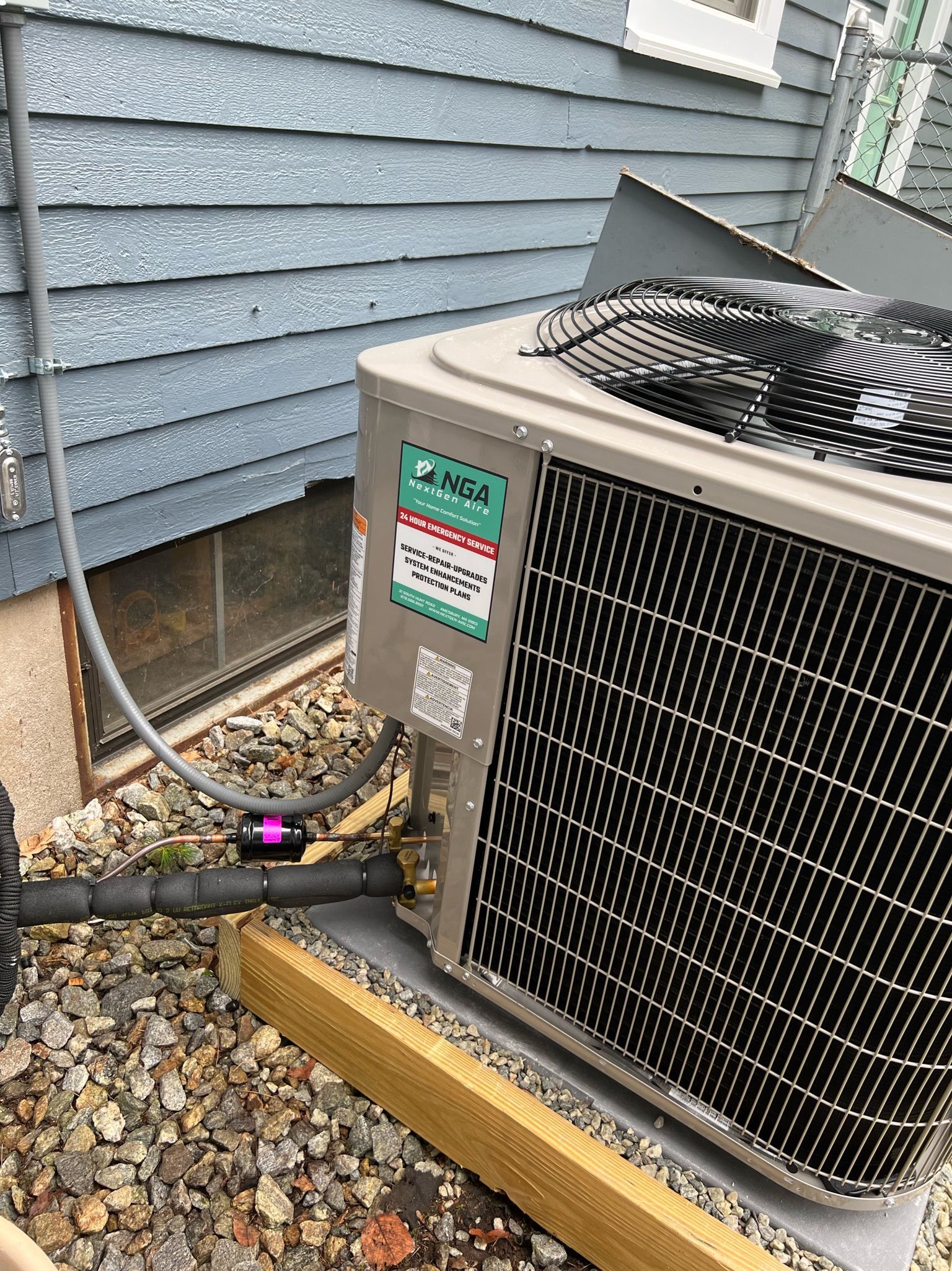 Air conditioning unit installed outside a house with blue siding.