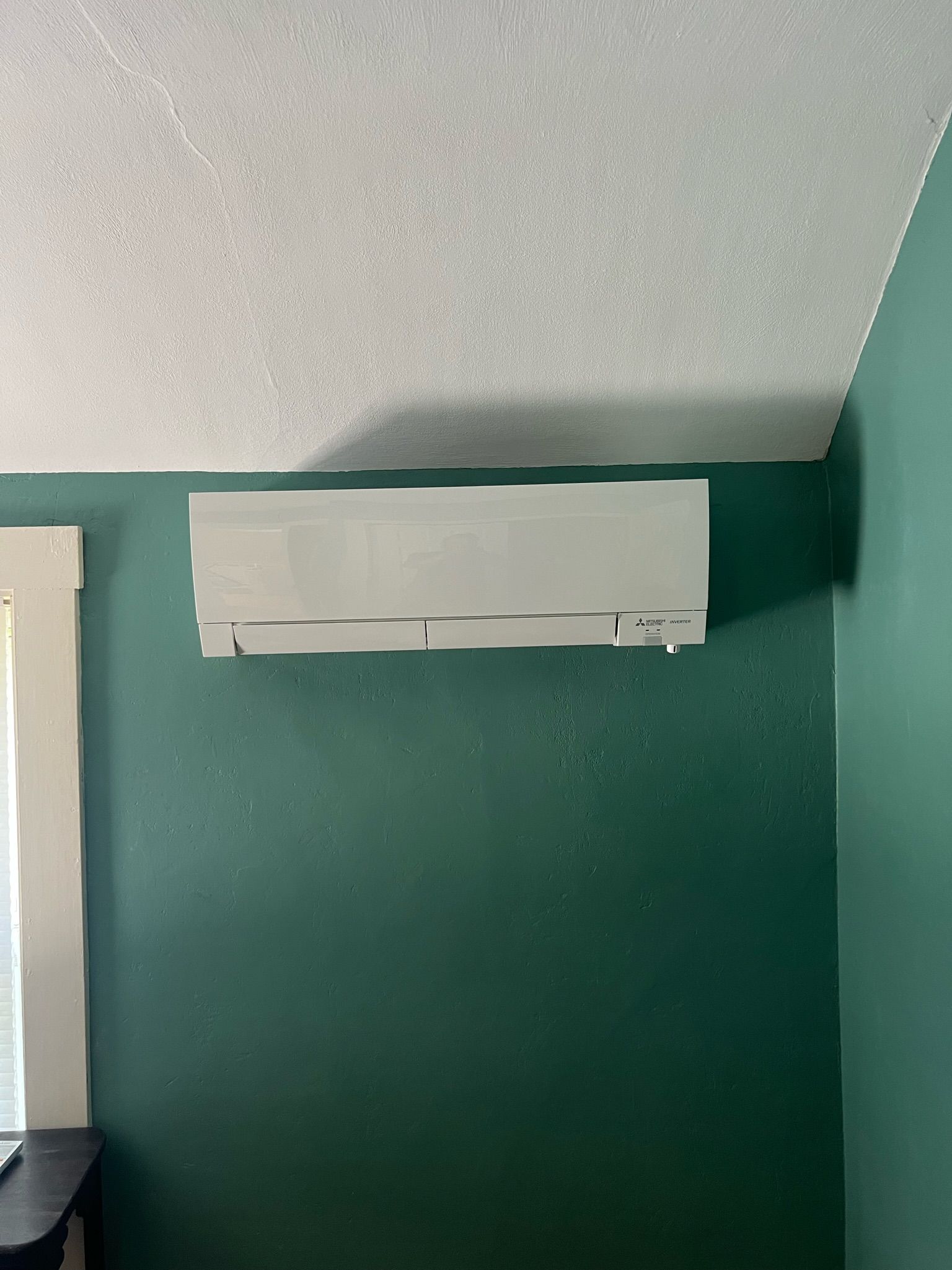 White wall-mounted air conditioner on a teal wall, near a white ceiling and corner.