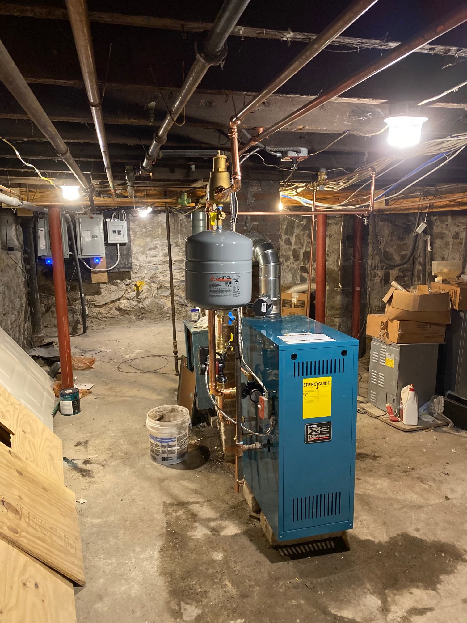 Blue boiler in a basement, with copper pipes and a grey expansion tank.