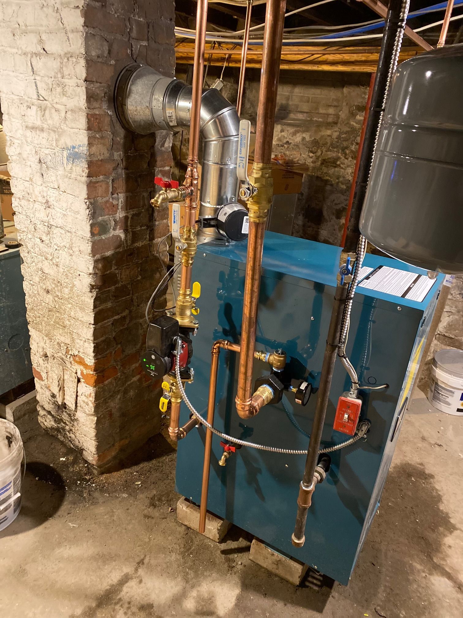 Blue heating boiler with copper pipes in a basement setting.